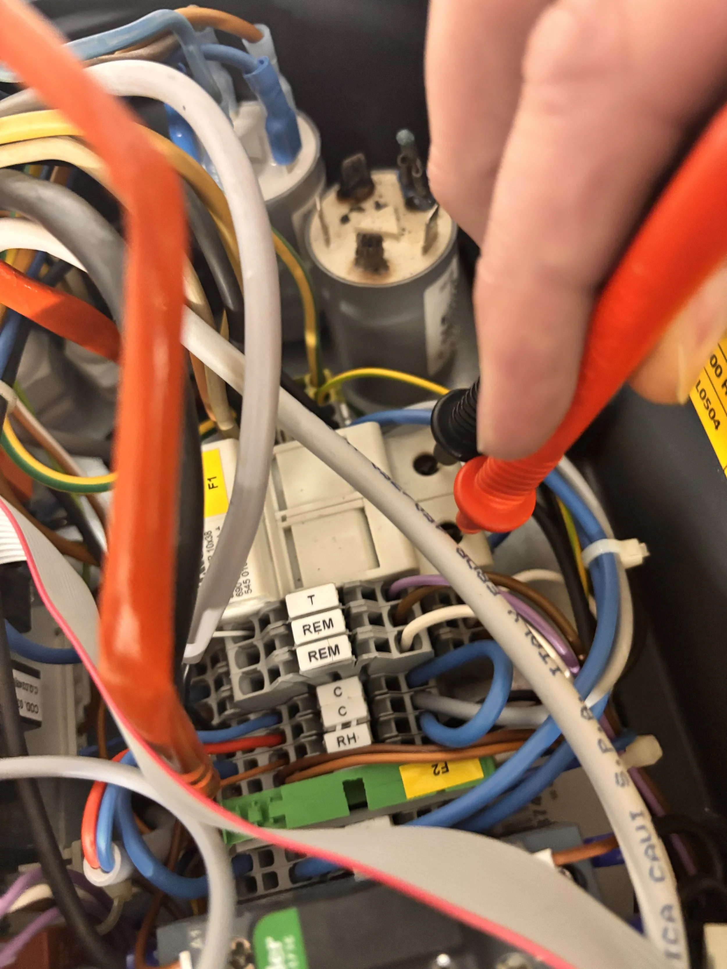 Close-up of an electrical wiring system with colorful wires, circuit components, and a person's hand using a screwdriver.