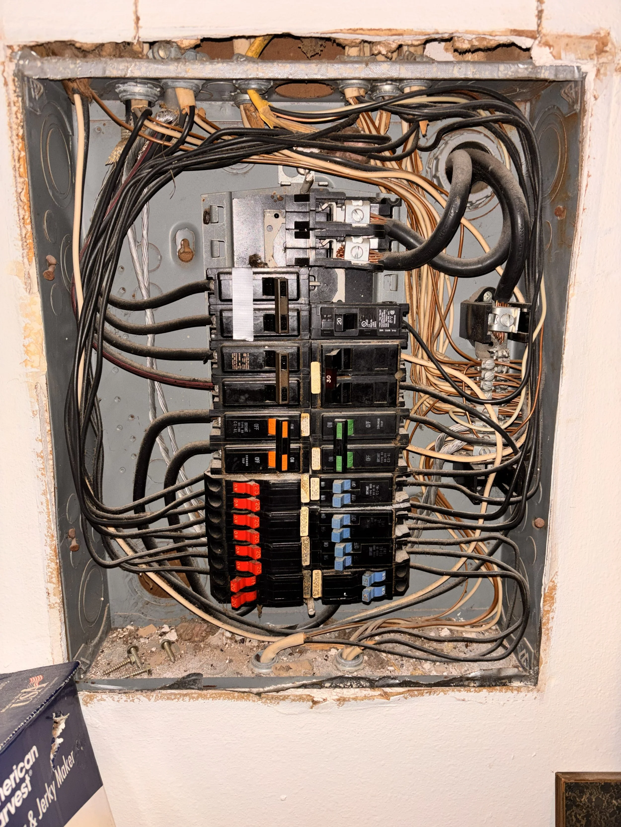 Open electrical breaker box with multiple circuit breakers and wiring inside a wall.