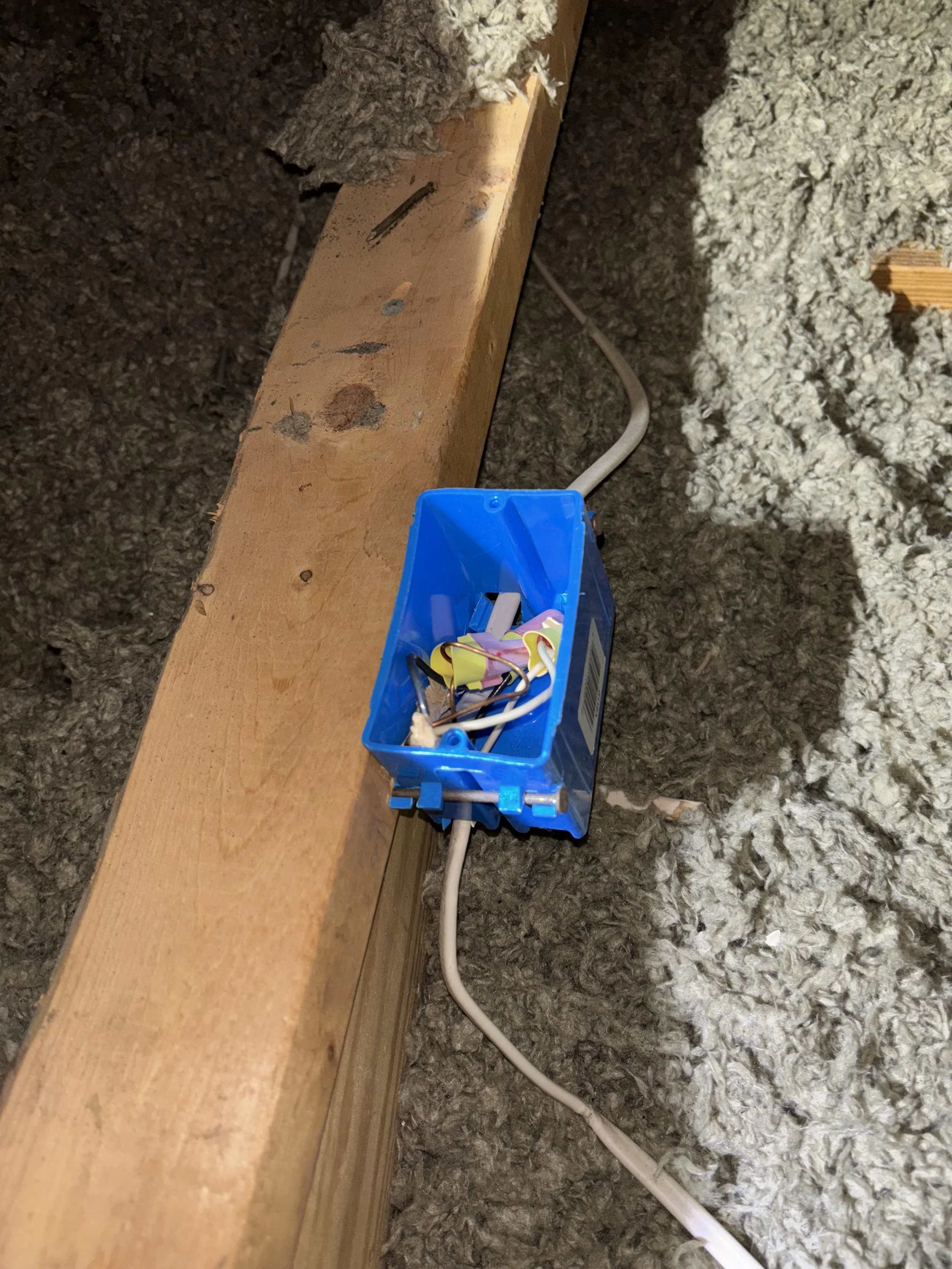 Electrical outlet box with disconnected wires, installed in a wooden beam with insulation around.
