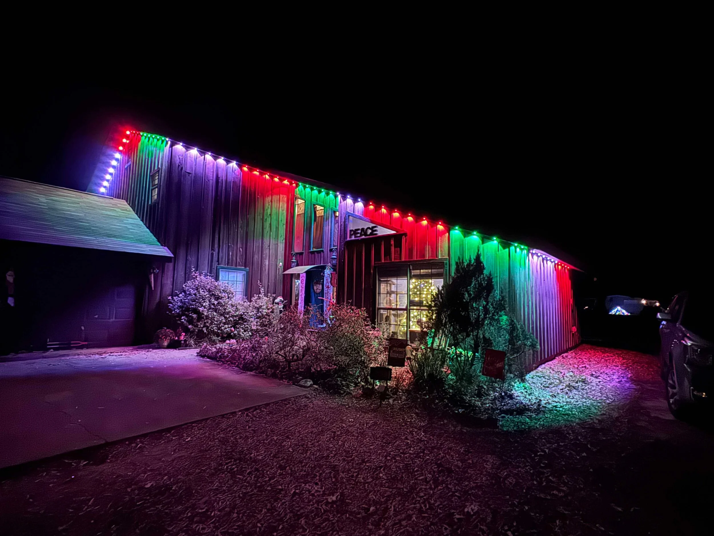 A house decorated with multi-colored Christmas lights at night, with a garden and a driveway in front.