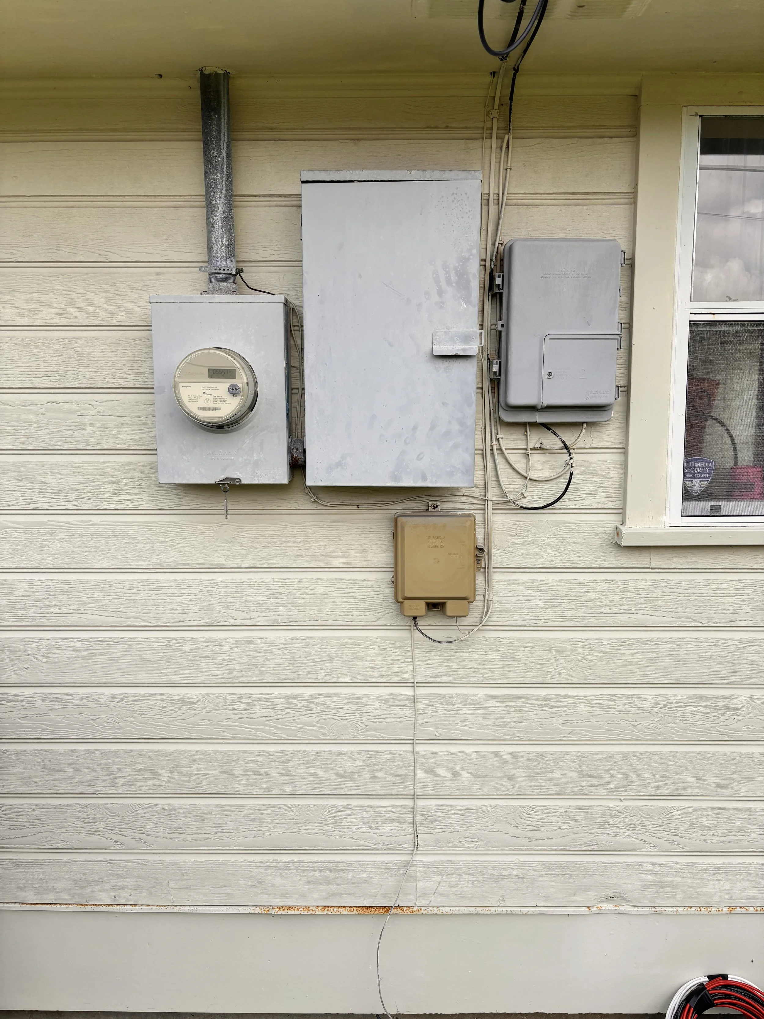 Exterior wall of a house with electrical meters, boxes, and wires.