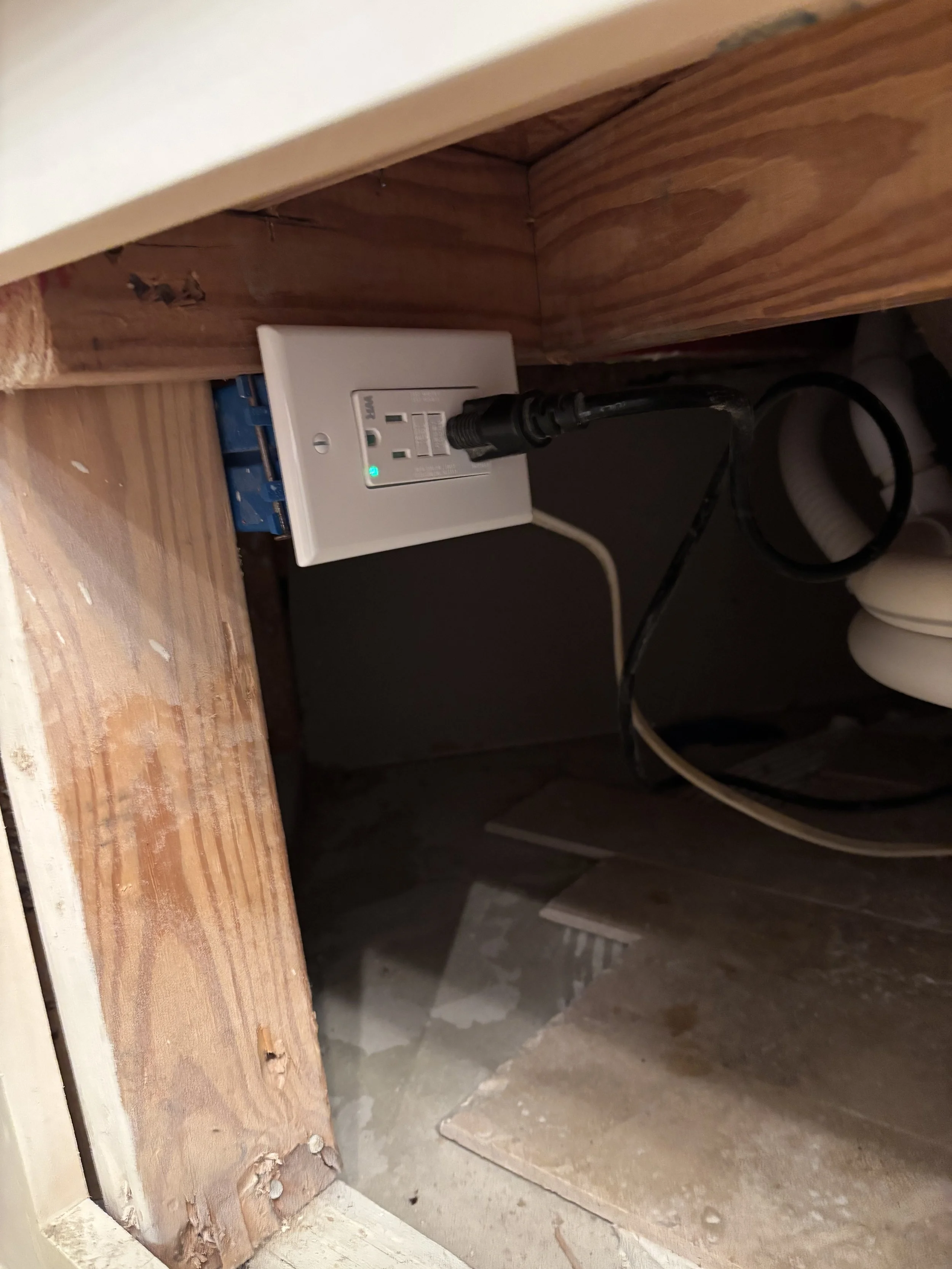 An electrical outlet in a wooden cabinet with a power strip plugged into it, and cords connected.