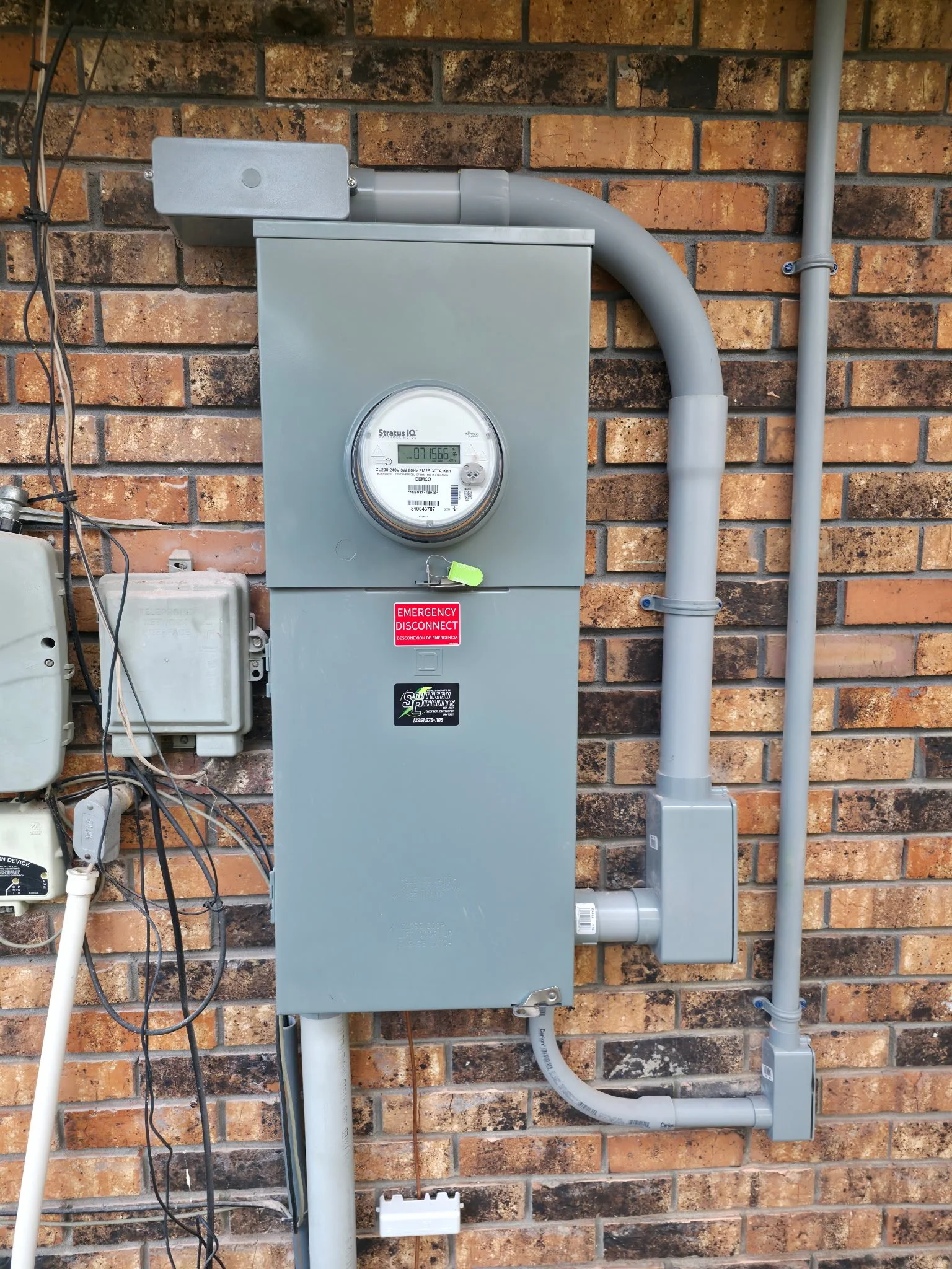 Exterior view of an electric meter box and electrical conduits mounted on a brick wall.