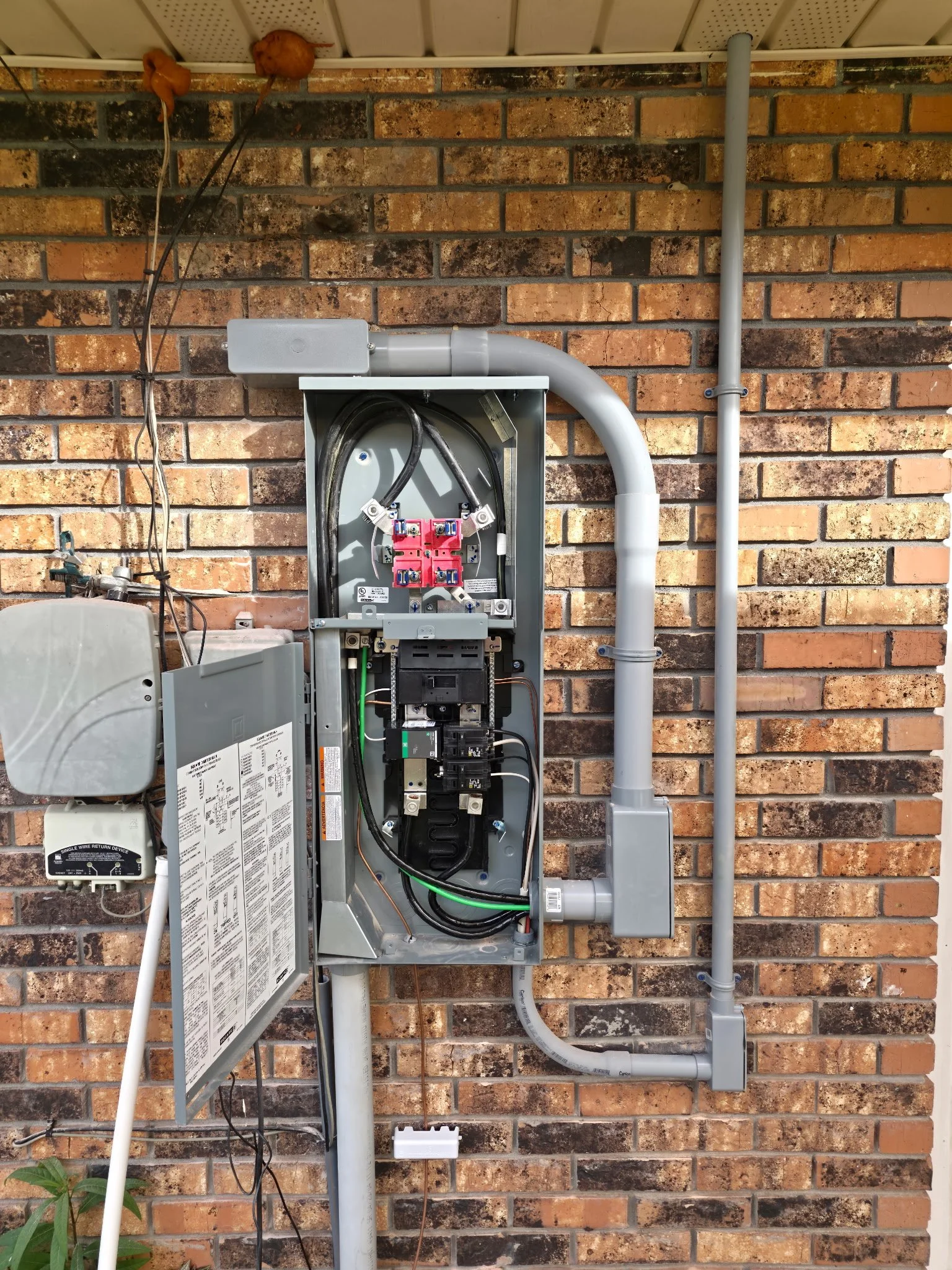 Open electrical meter box with wiring and circuit breakers on a brick wall.