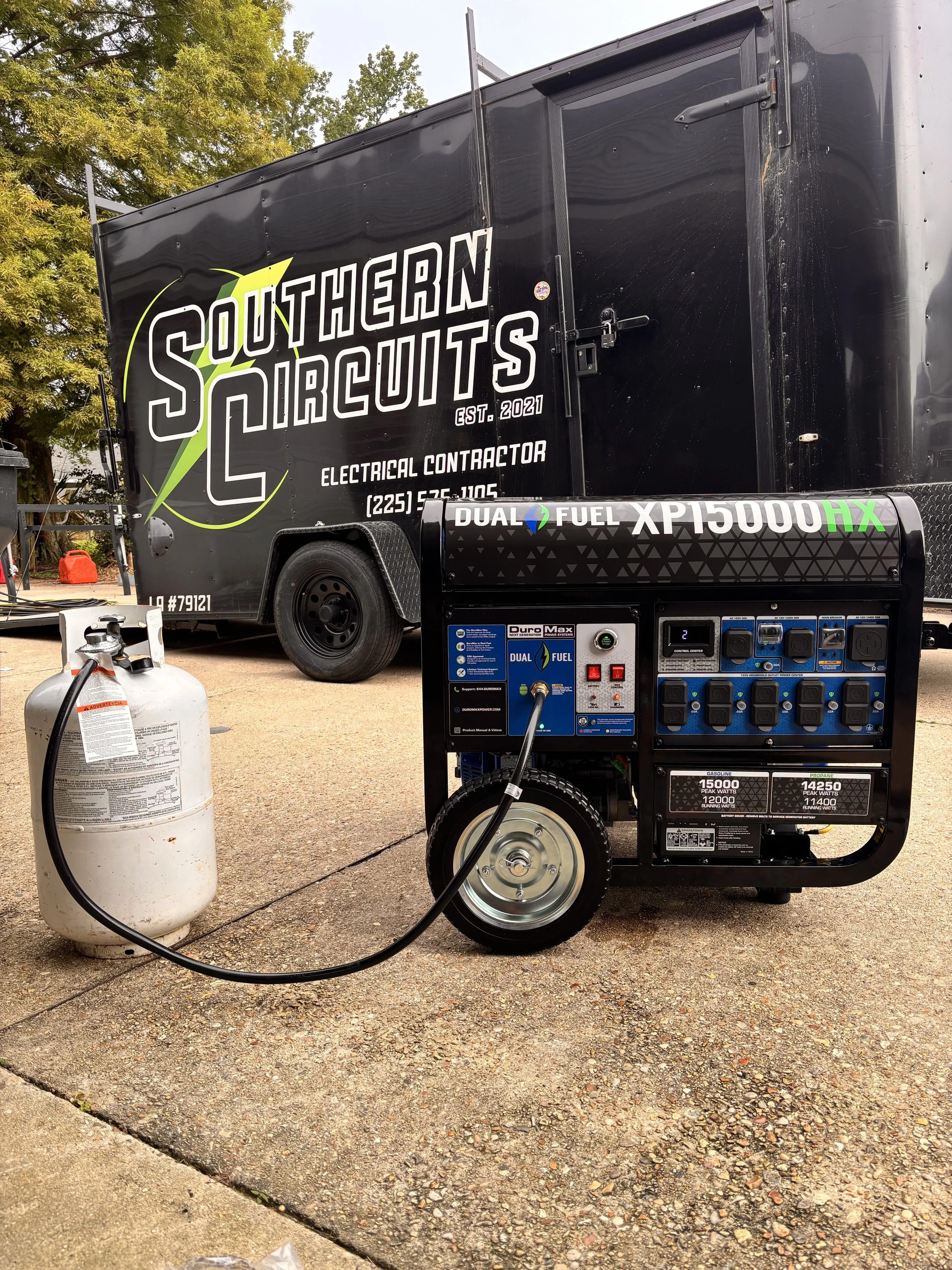 A portable dual fuel generator connected to a propane tank in front of a black trailer marked 'Southern Circuits' with contact information and information about electrical contracting services.