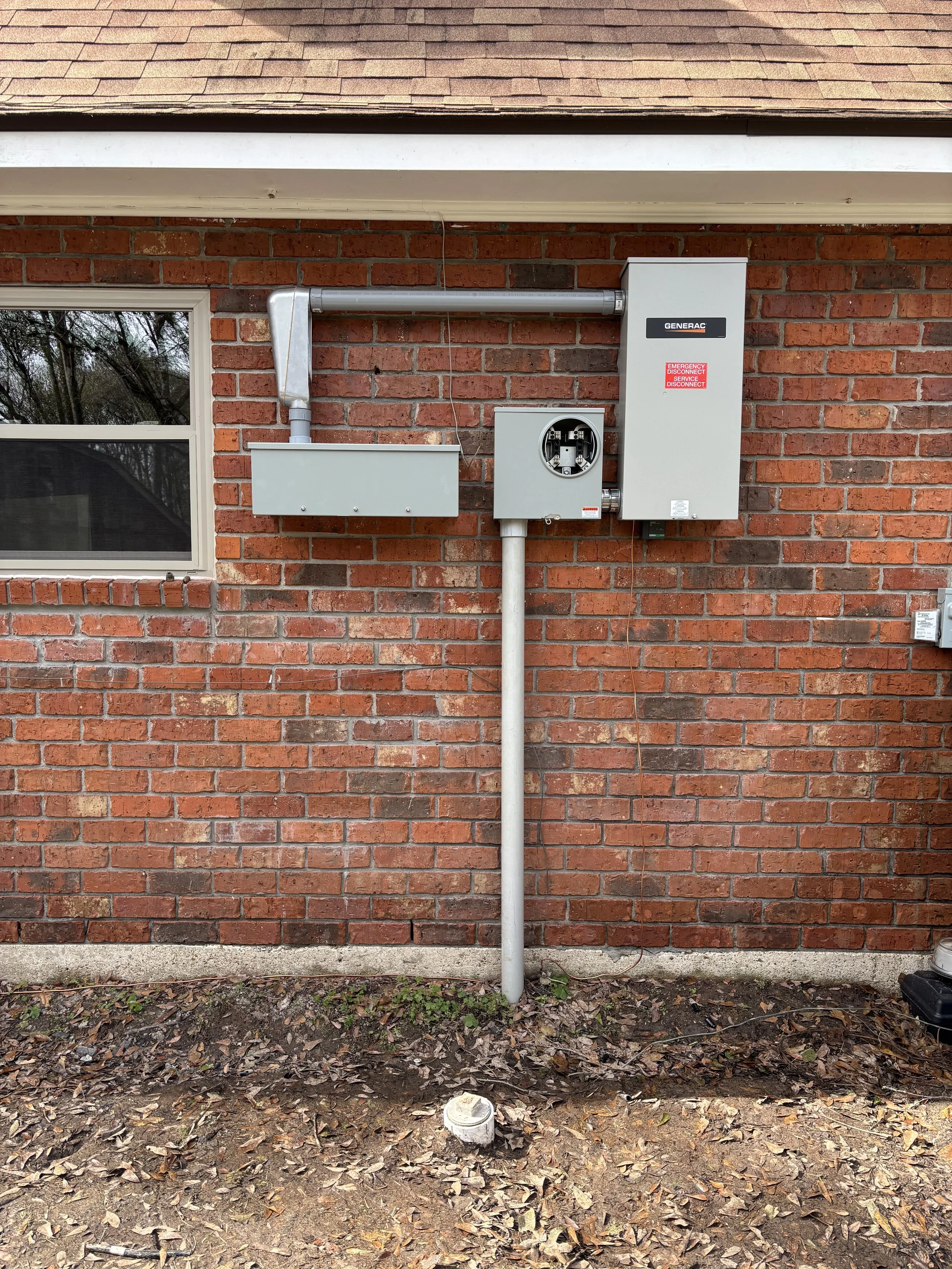 Electrical meters and panels installed outside a brick house, with a small window and debris on the ground.