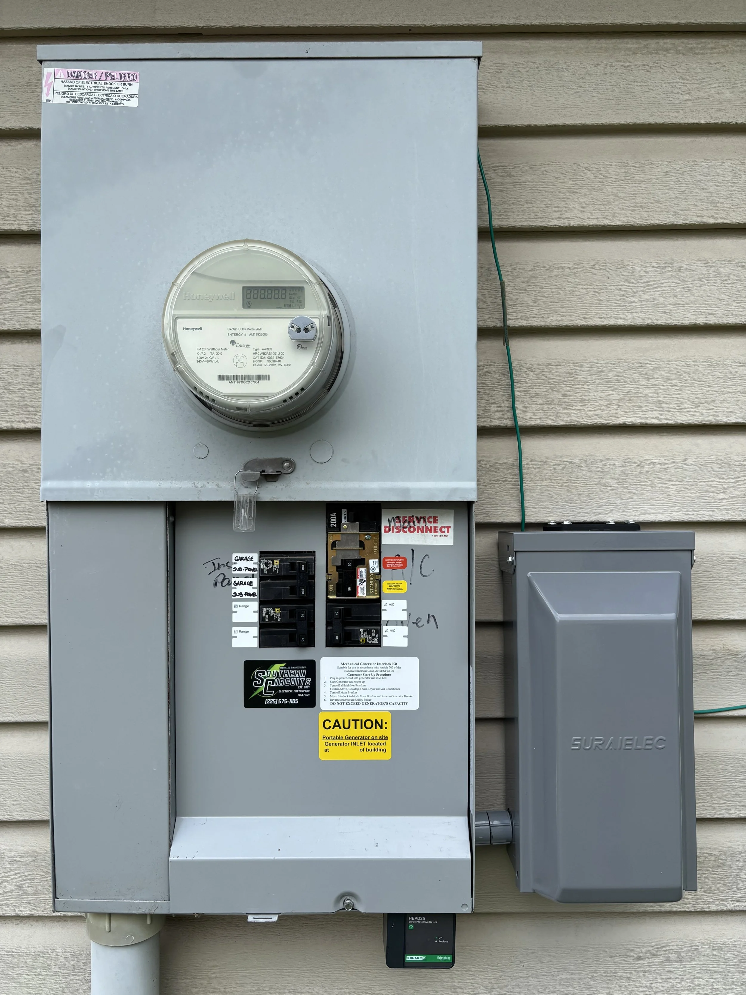Electric meter, circuit breaker panel, and electrical box mounted outside a building with siding.