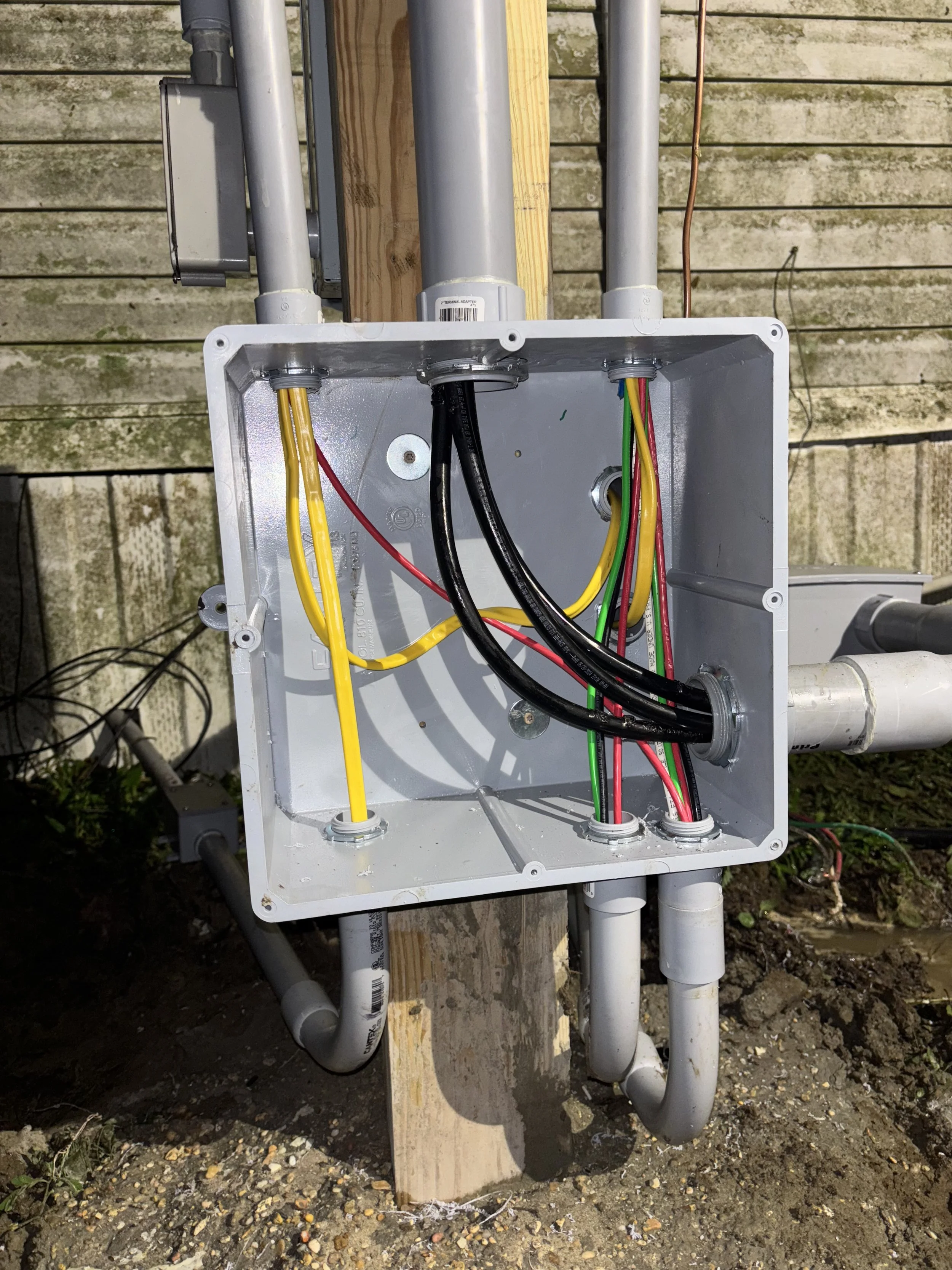 Open electrical box with various color-coded wires and conduits installed on a wooden utility pole outdoors.