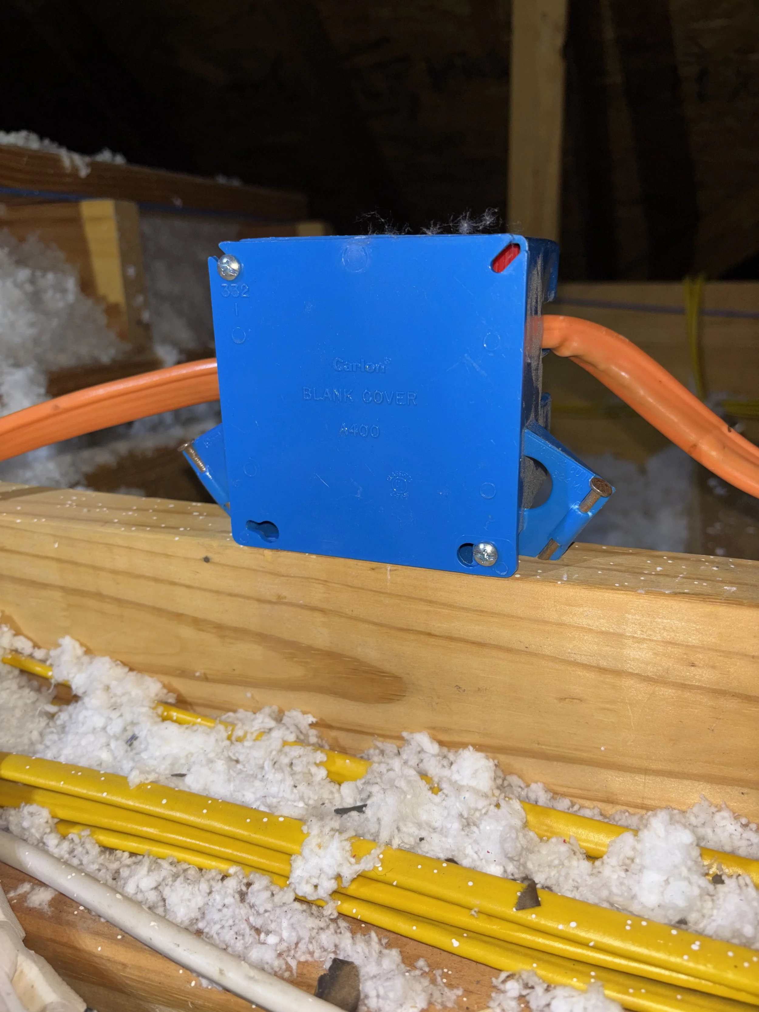 Blue electrical switch box with orange conduit, installed in an attic with wood framing and insulation.