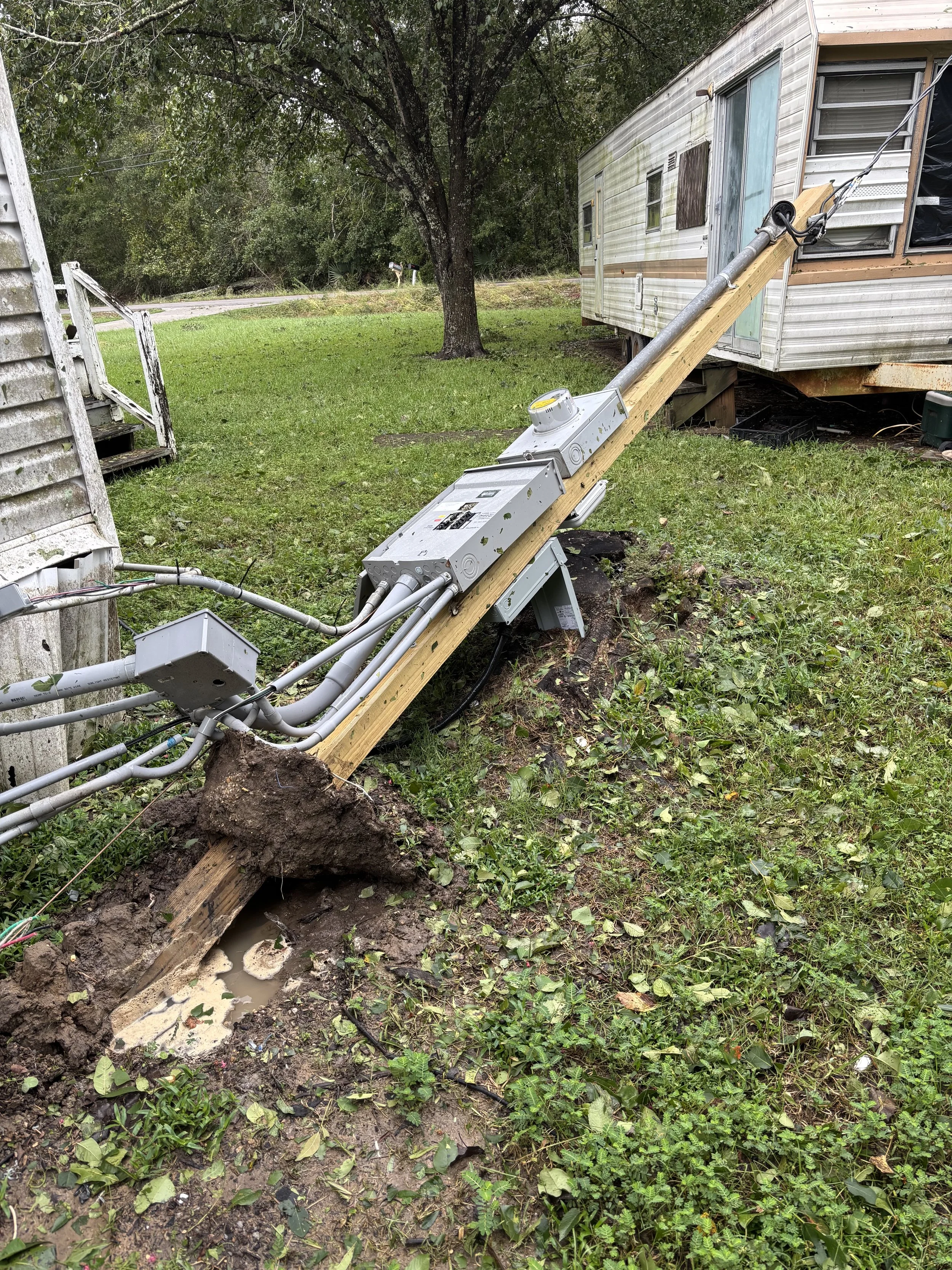 Installation of electrical or utility equipment with conduit pipes and control boxes on a wooden support near a mobile home in a grassy outdoor setting.