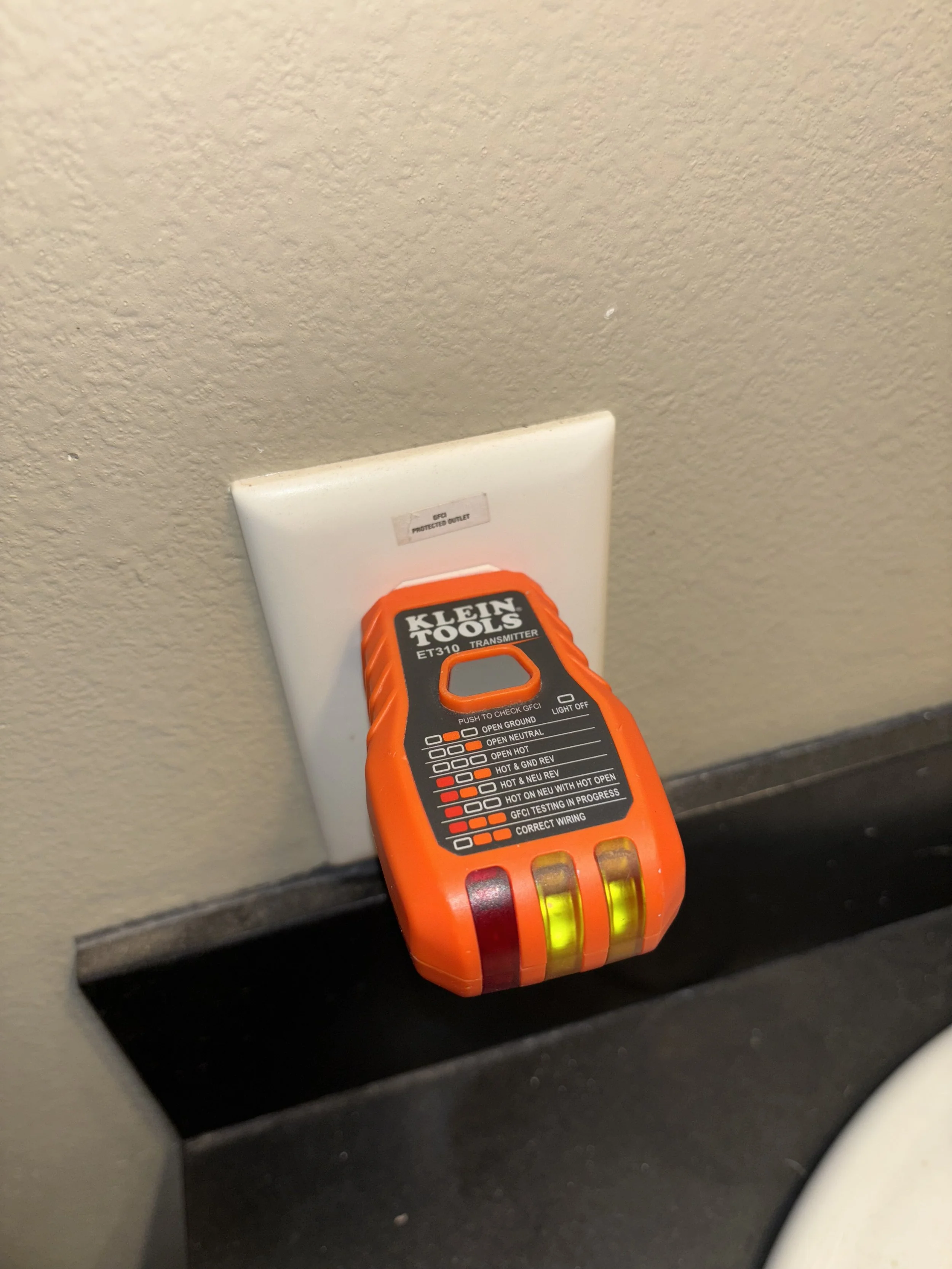 A Klein Tools ET310 transmitter plugged into an electrical outlet, with indicator lights on, used for testing electrical wiring.