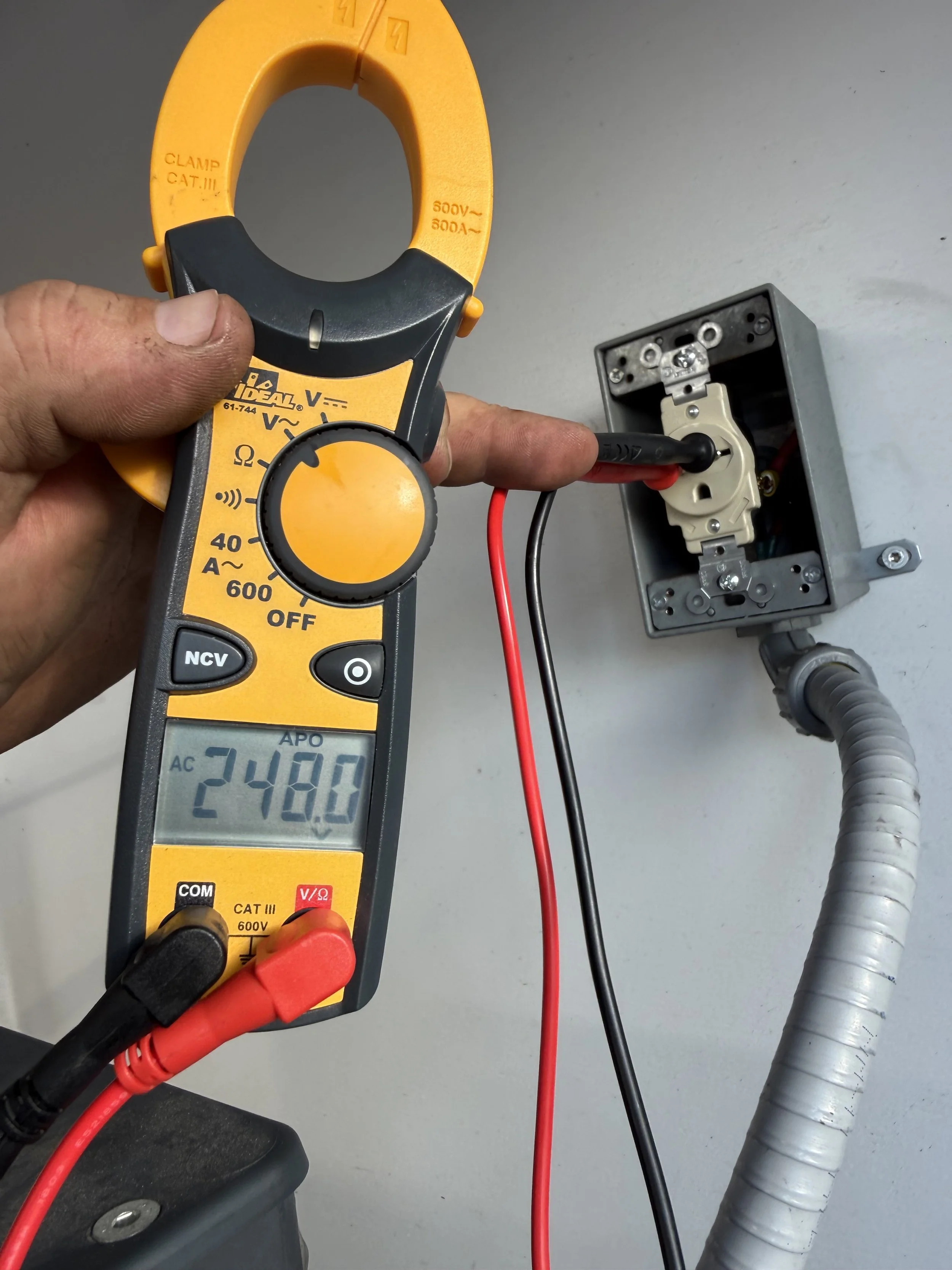 A digital clamp meter testing a wall electrical outlet, displaying a reading of 248.0 volts.
