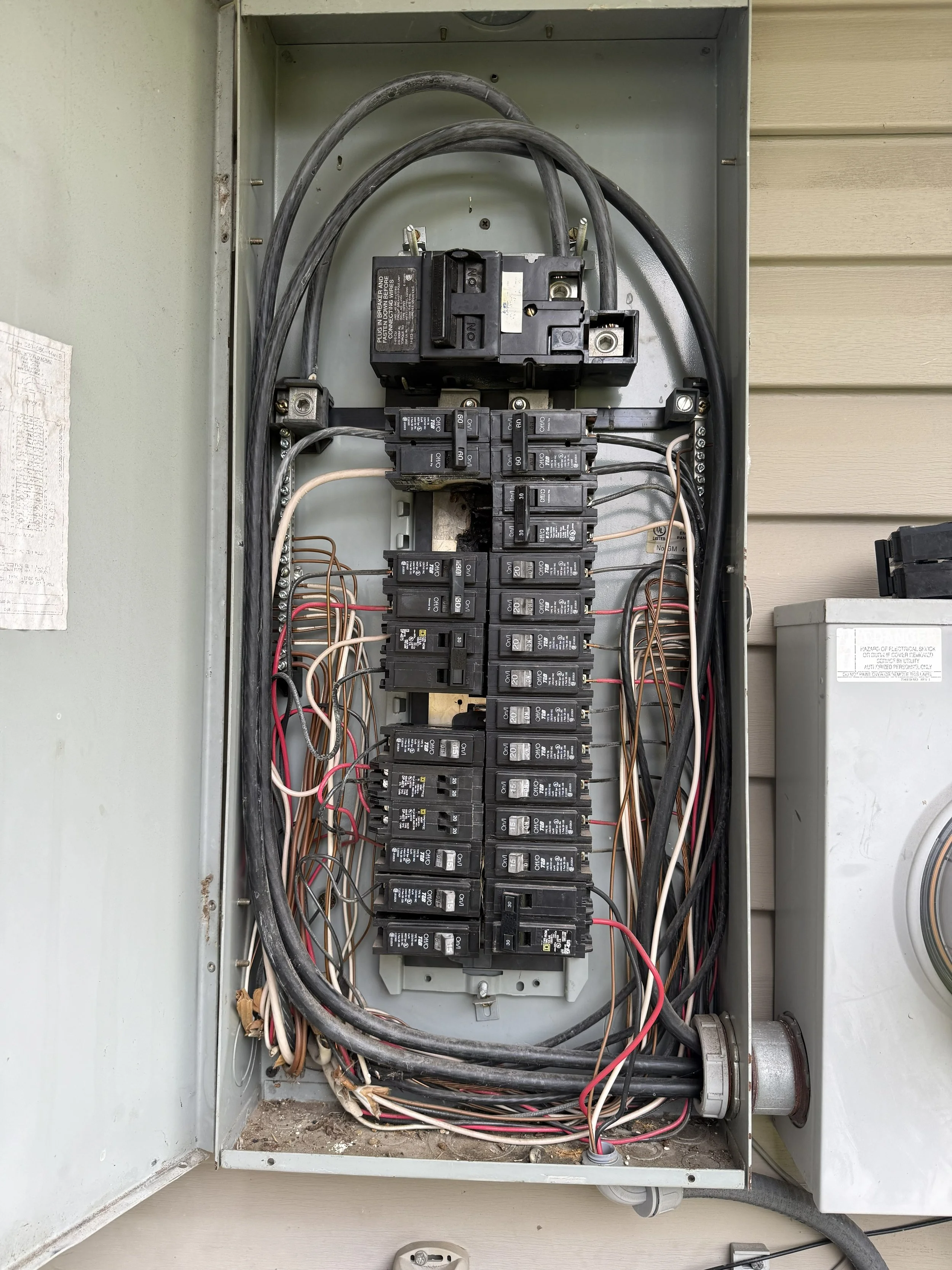 An open electrical breaker box with multiple circuit breakers and wiring inside.