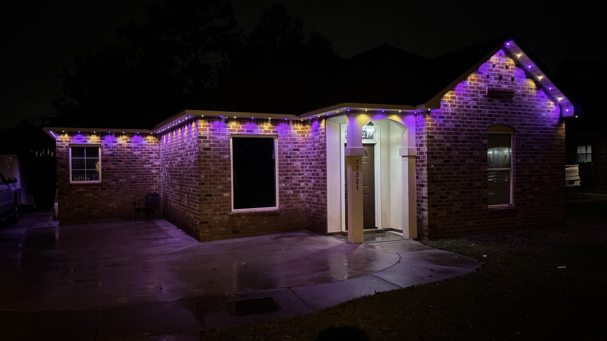 A brick house at night decorated with purple and yellow Christmas lights along the roofline.