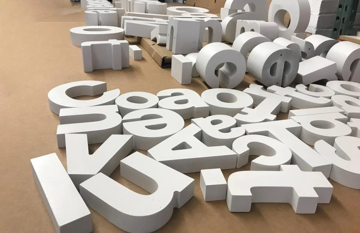 Letras grandes y blancas dispersas en el suelo de un espacio interior de almacén o taller.