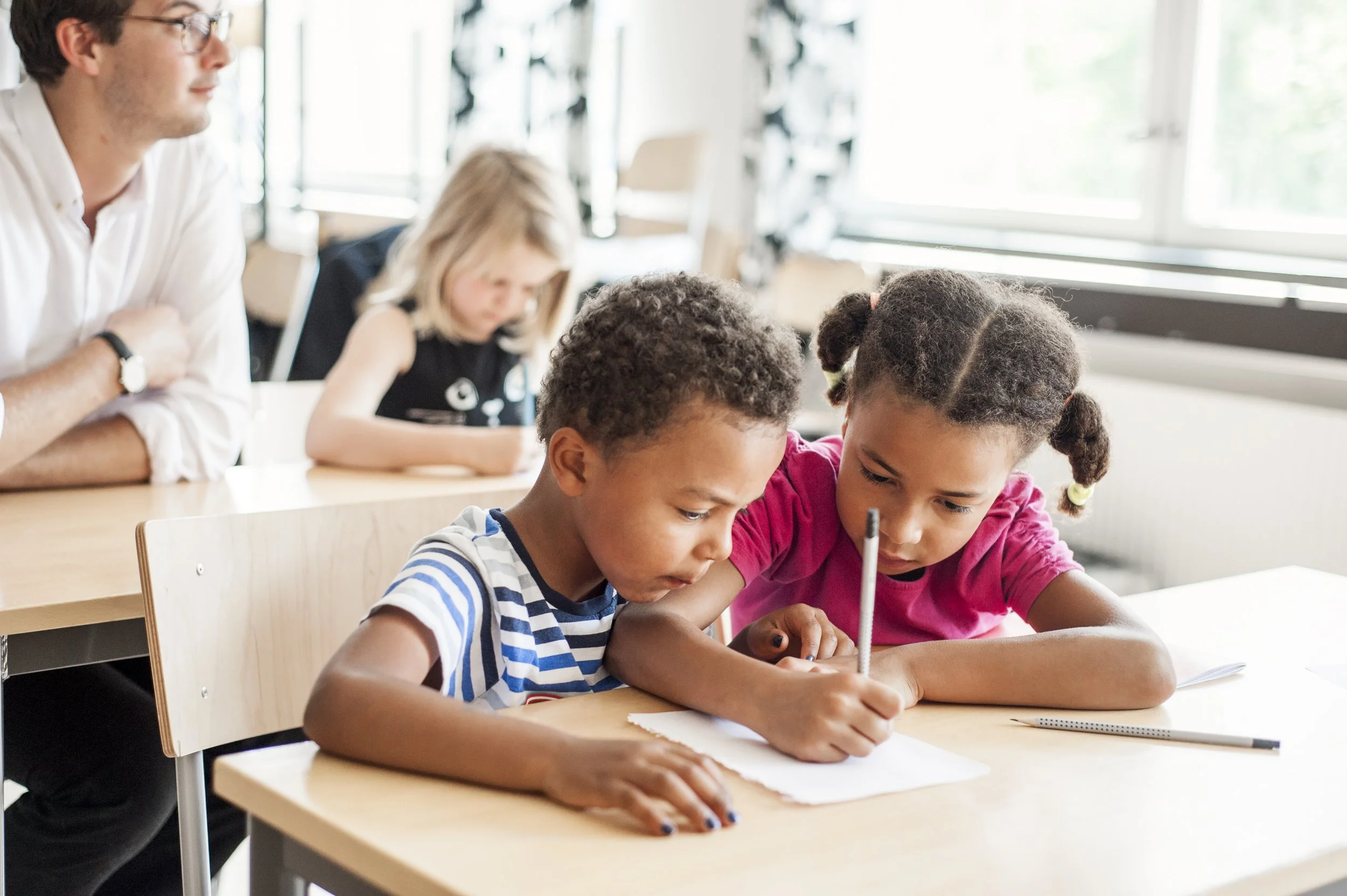 two young children, sitting at a desk writing.