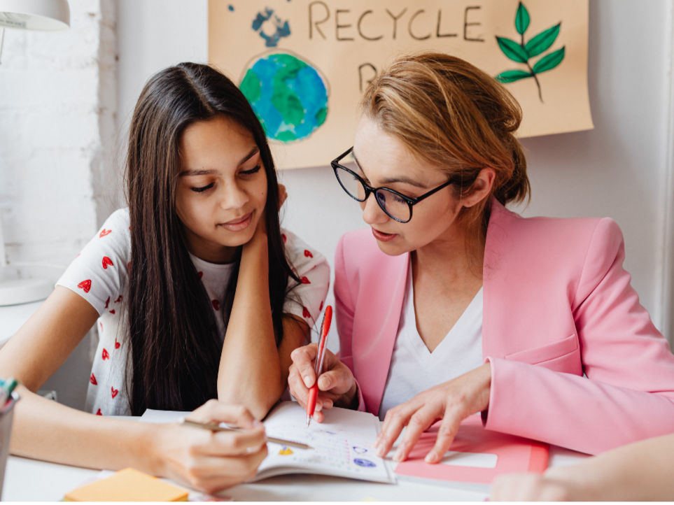 a student and teacher looking at a school workbook together.