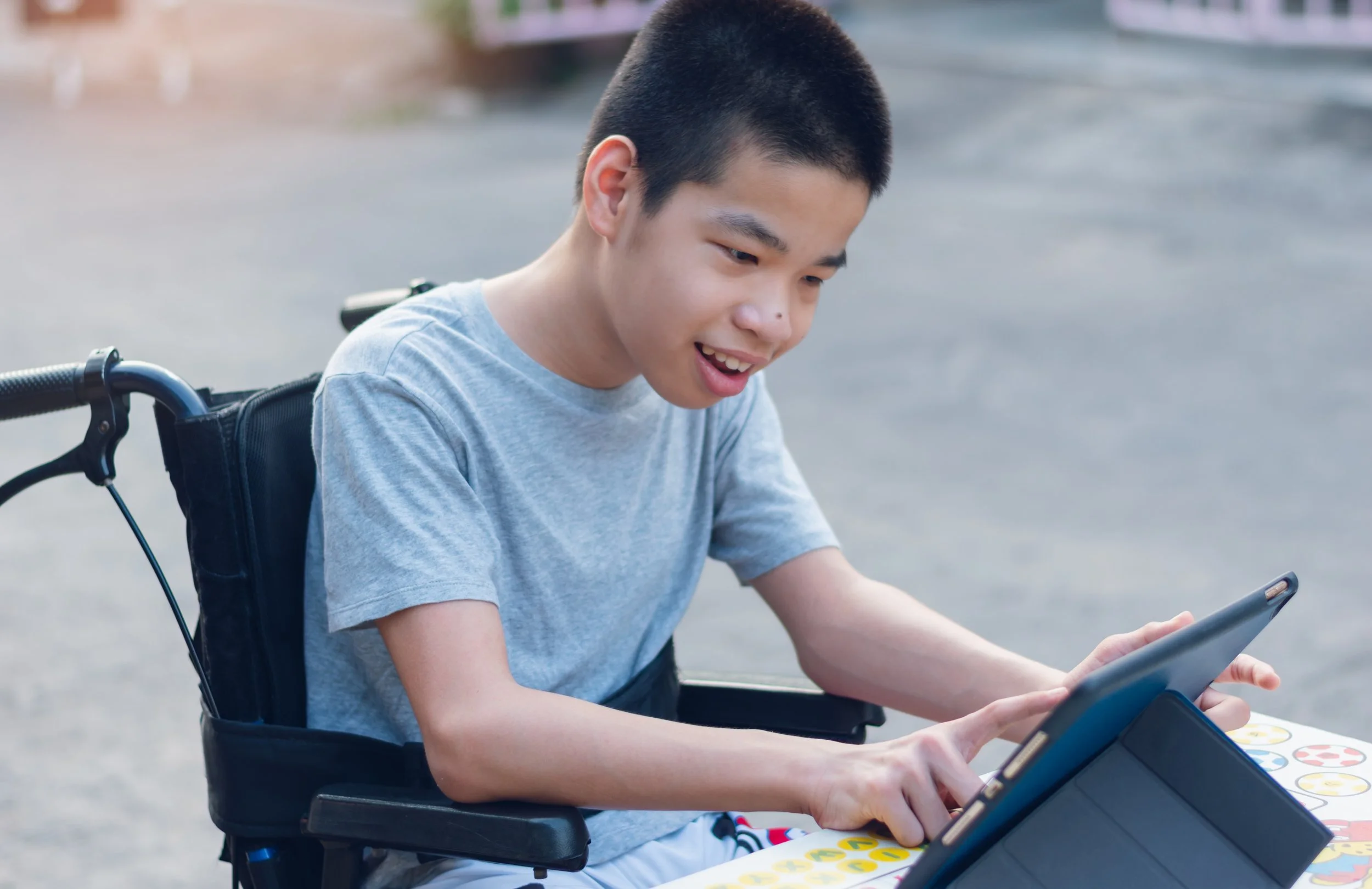 a young asian boy in a wheelchair using a tablet.