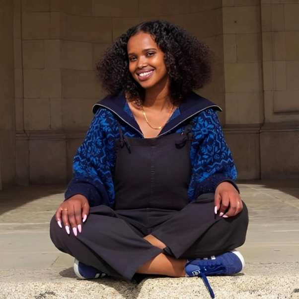A picture of Warda, a black woman sitting on the floor crossed legged, smiling. 