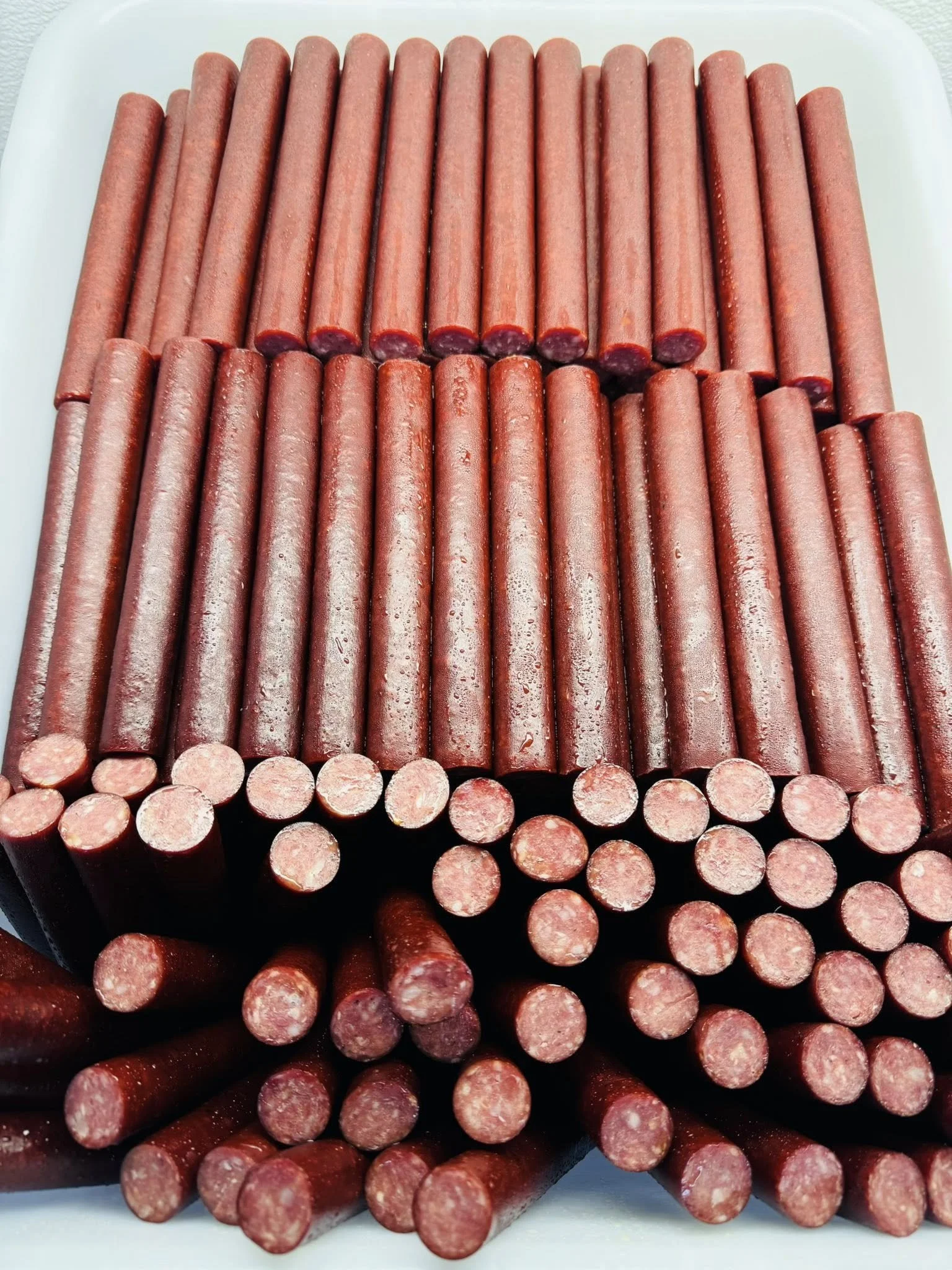 A tray filled with uncooked hot dogs arranged in a grid pattern.