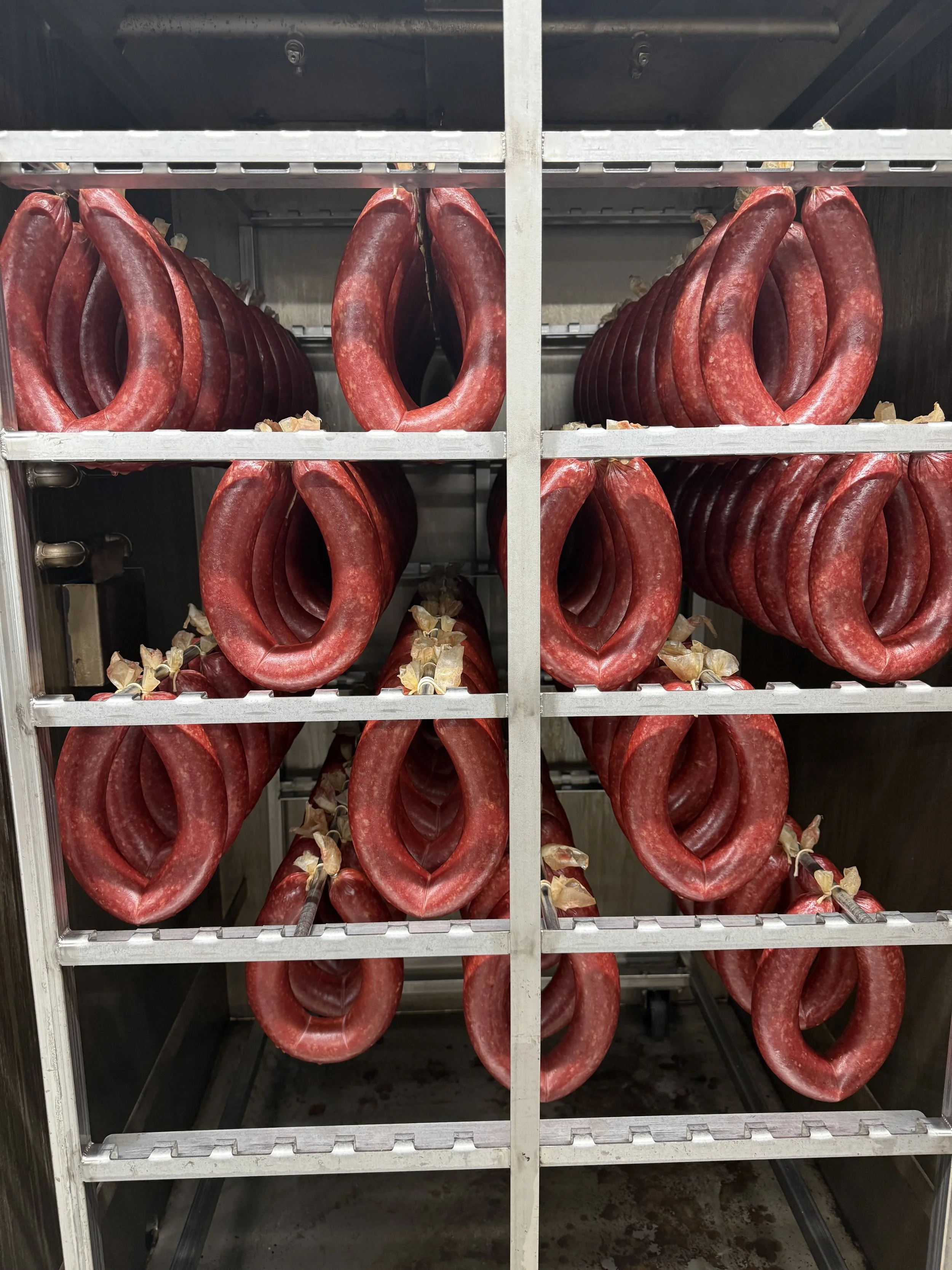 Red sausage loops hanging on a metal rack in a food processing or storage area.