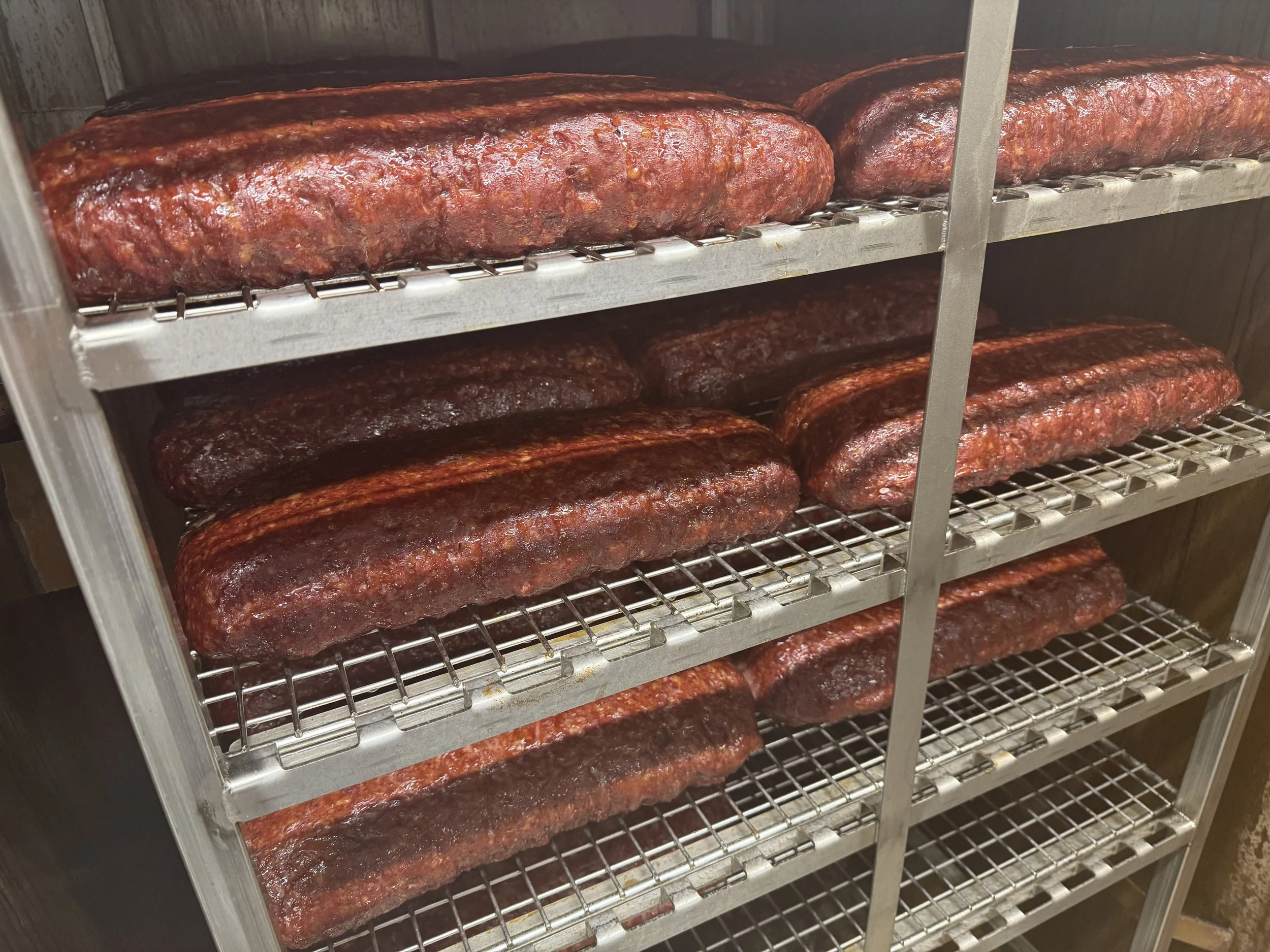 Several racks of smoked or cooked barbecue briskets on metal shelves in a smoker or storage unit.