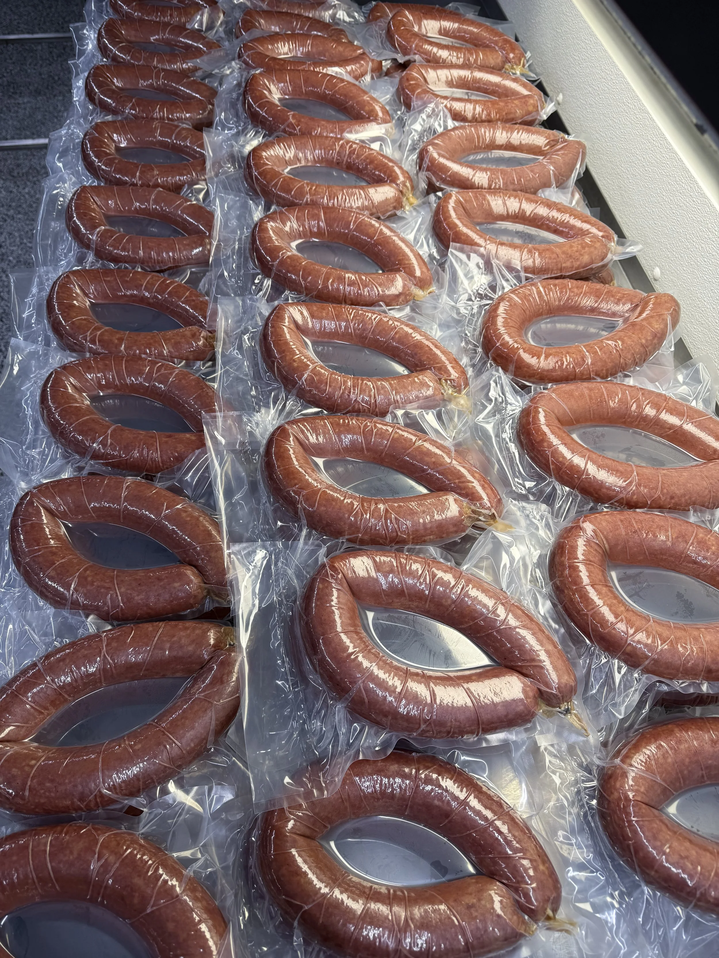 Several large, ring-shaped sausages on a surface, each sealed in clear plastic packaging.
