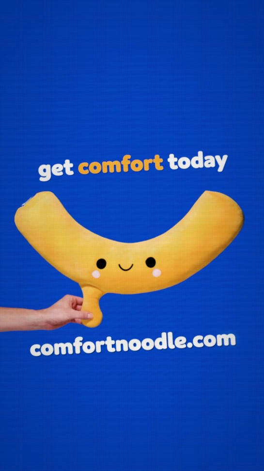 Blue background with a plush banana character smiling and a hand holding its stem. Text says 'get comfort today' and 'comfortnoodle.com'.