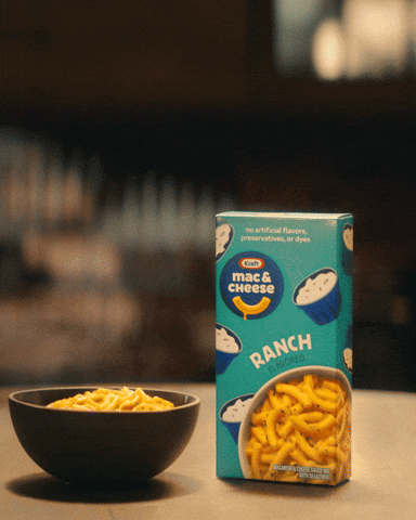 A bowl of macaroni and cheese next to a carton of Kraft Mac & Cheese Ranch flavored pasta on a table.