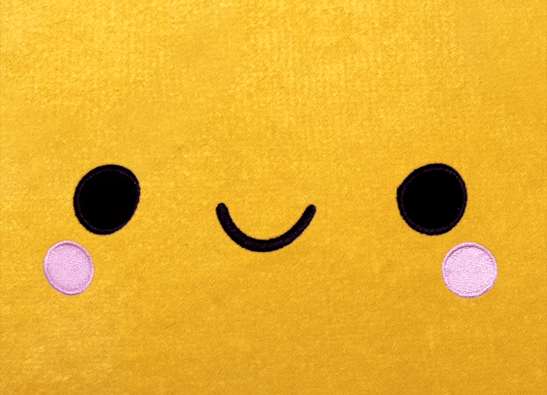 Close-up of a yellow plush toy with a smiling face, black eyes, pink cheeks, and a simple black mouth.