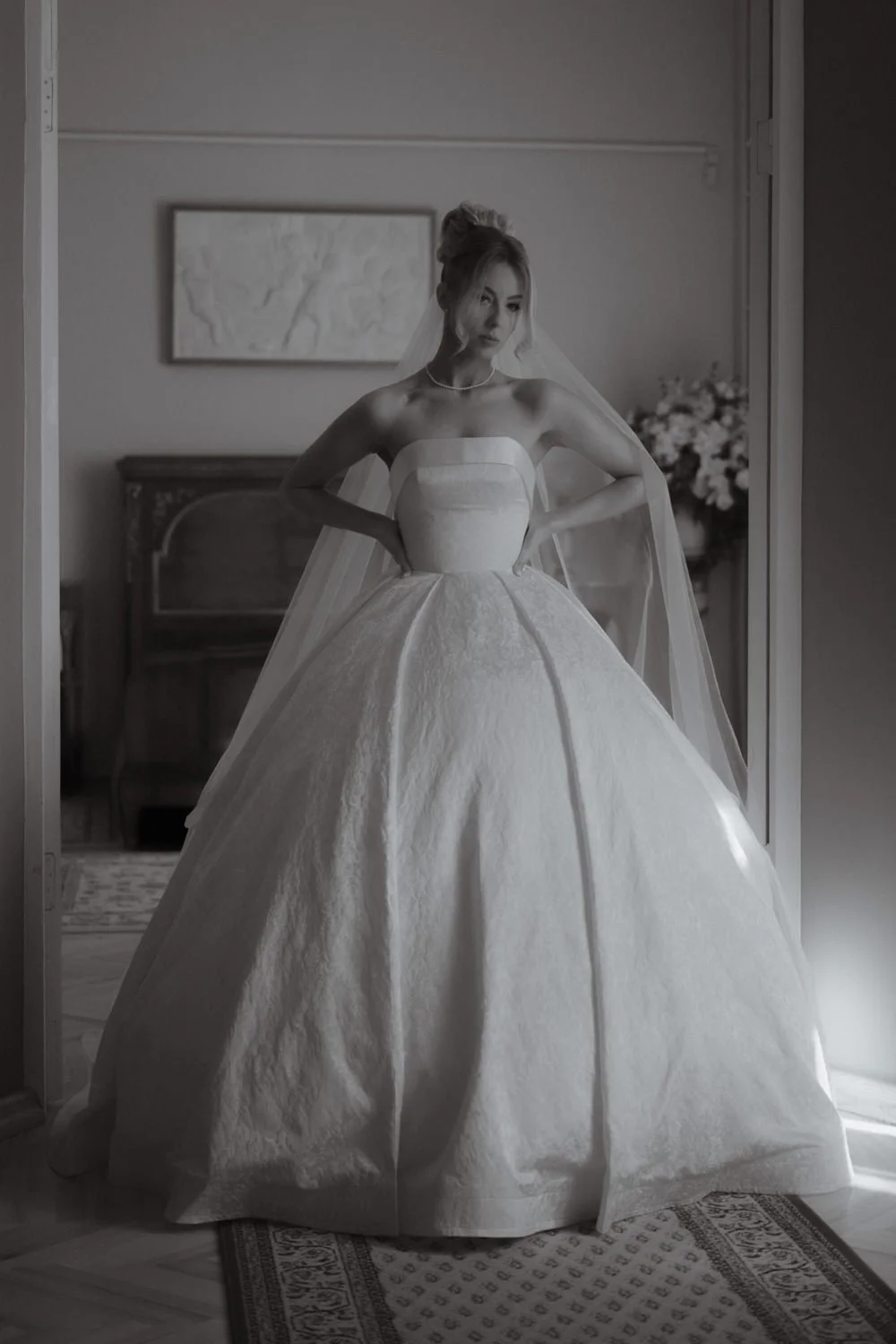 A woman in a wedding gown standing in a room with hands on her hips.