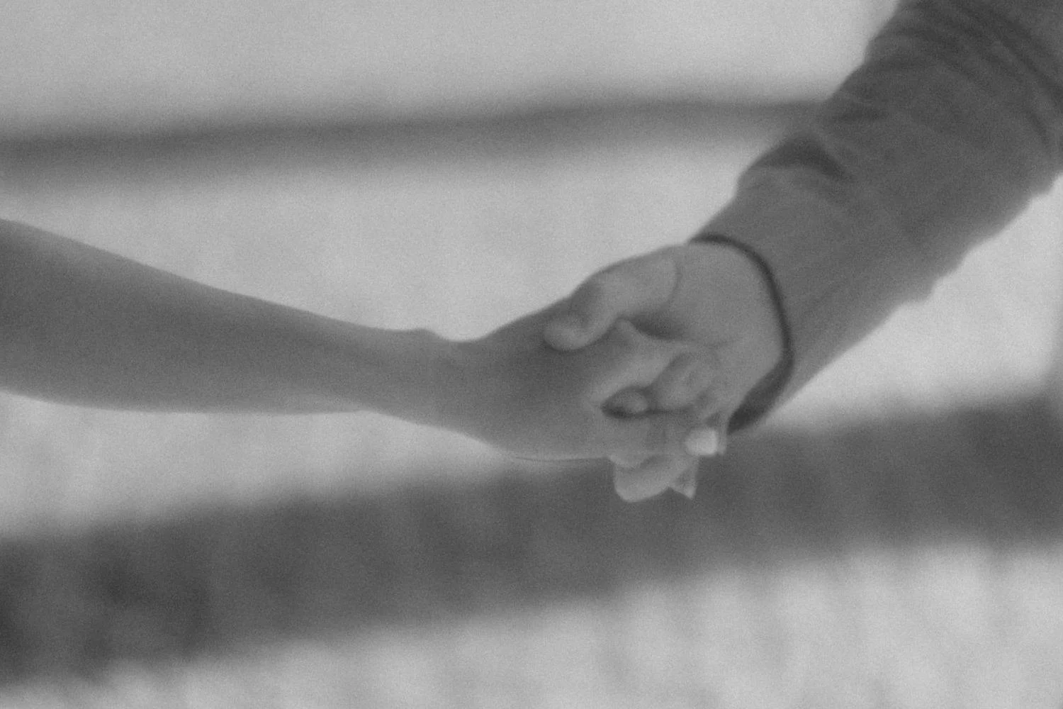 Close-up of two people holding hands, one with a bracelet, in black and white.