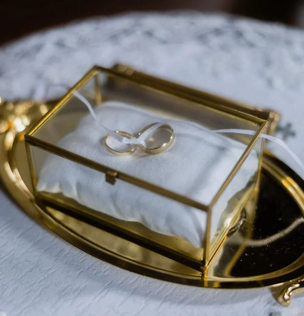 A pair of wedding rings in a glass display box on a white cushion.