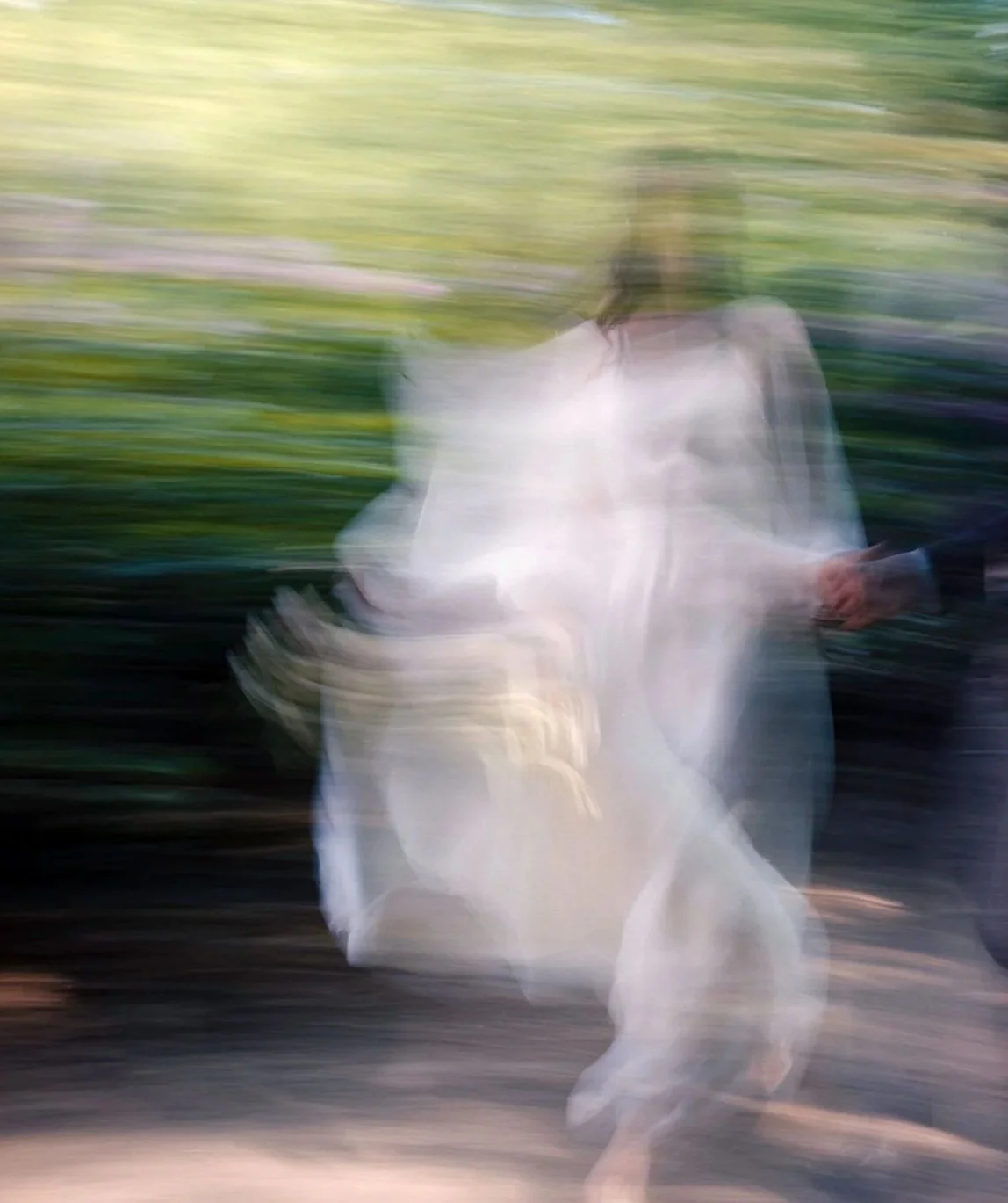 A person wearing white sitting outdoors with a background of green foliage, captured with motion blur.
