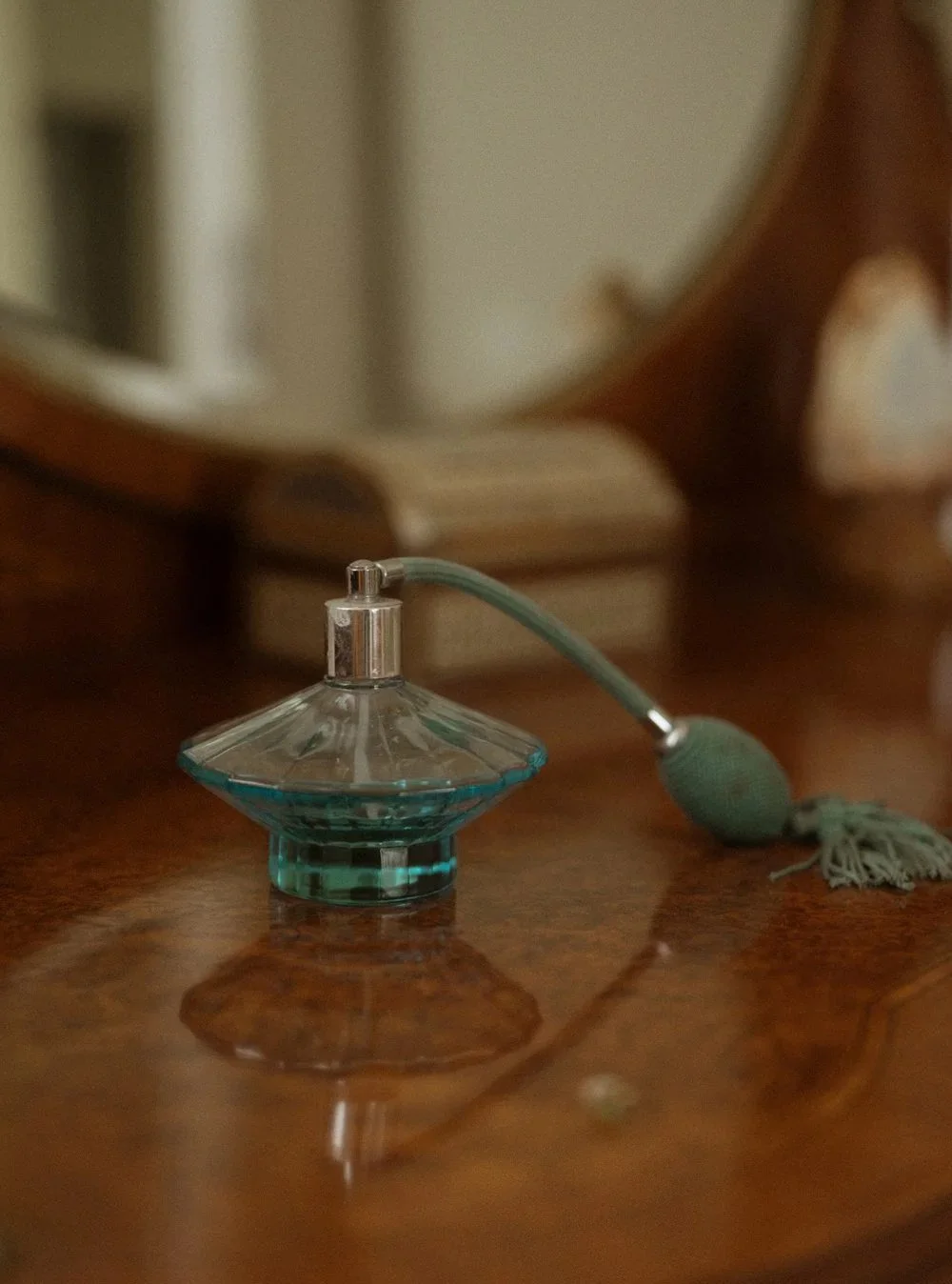 Vintage glass perfume bottle with a spray nozzle and tassel placed on a polished wooden surface.