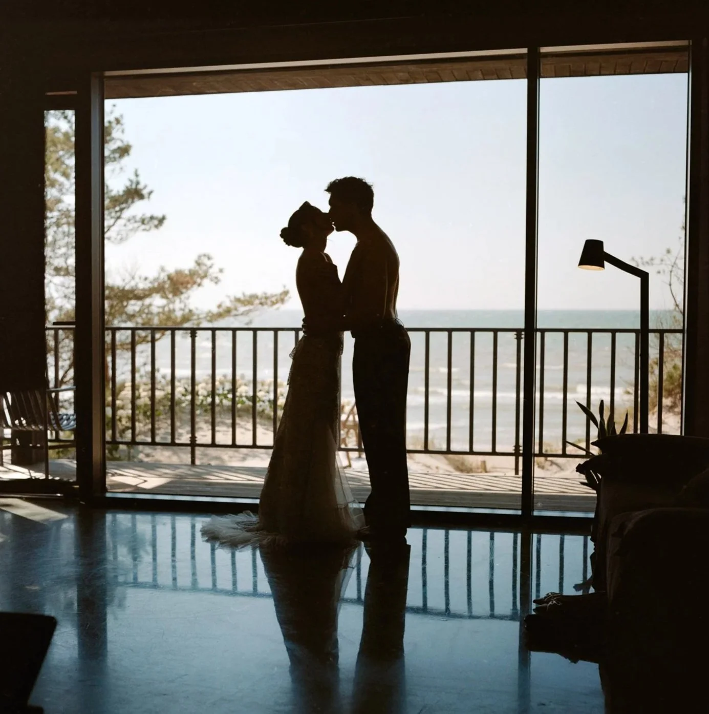 Silhouette of a couple kissing on a balcony overlooking the beach with the ocean in the background.