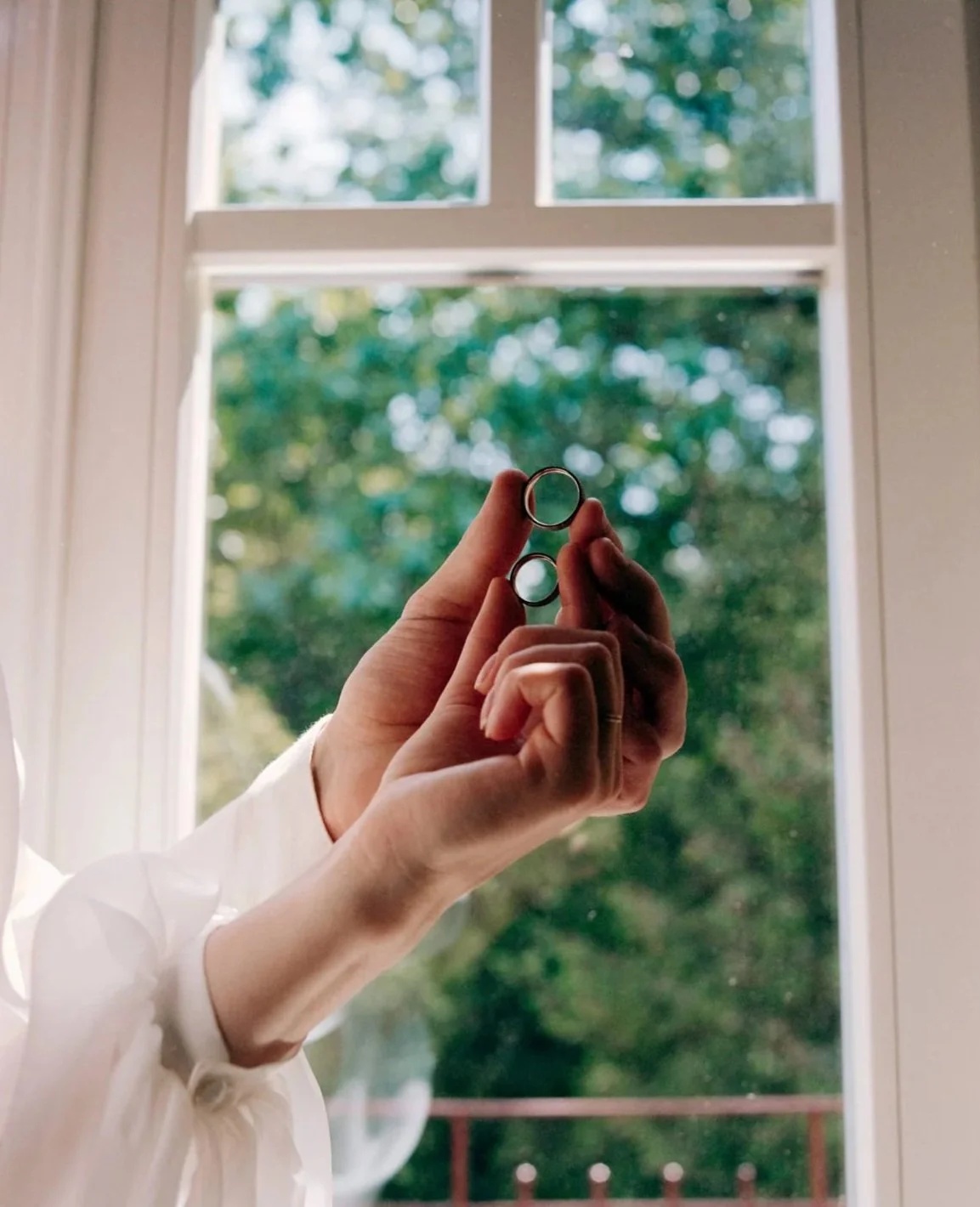 Person holding two interlocking rings near a window with green trees outside.