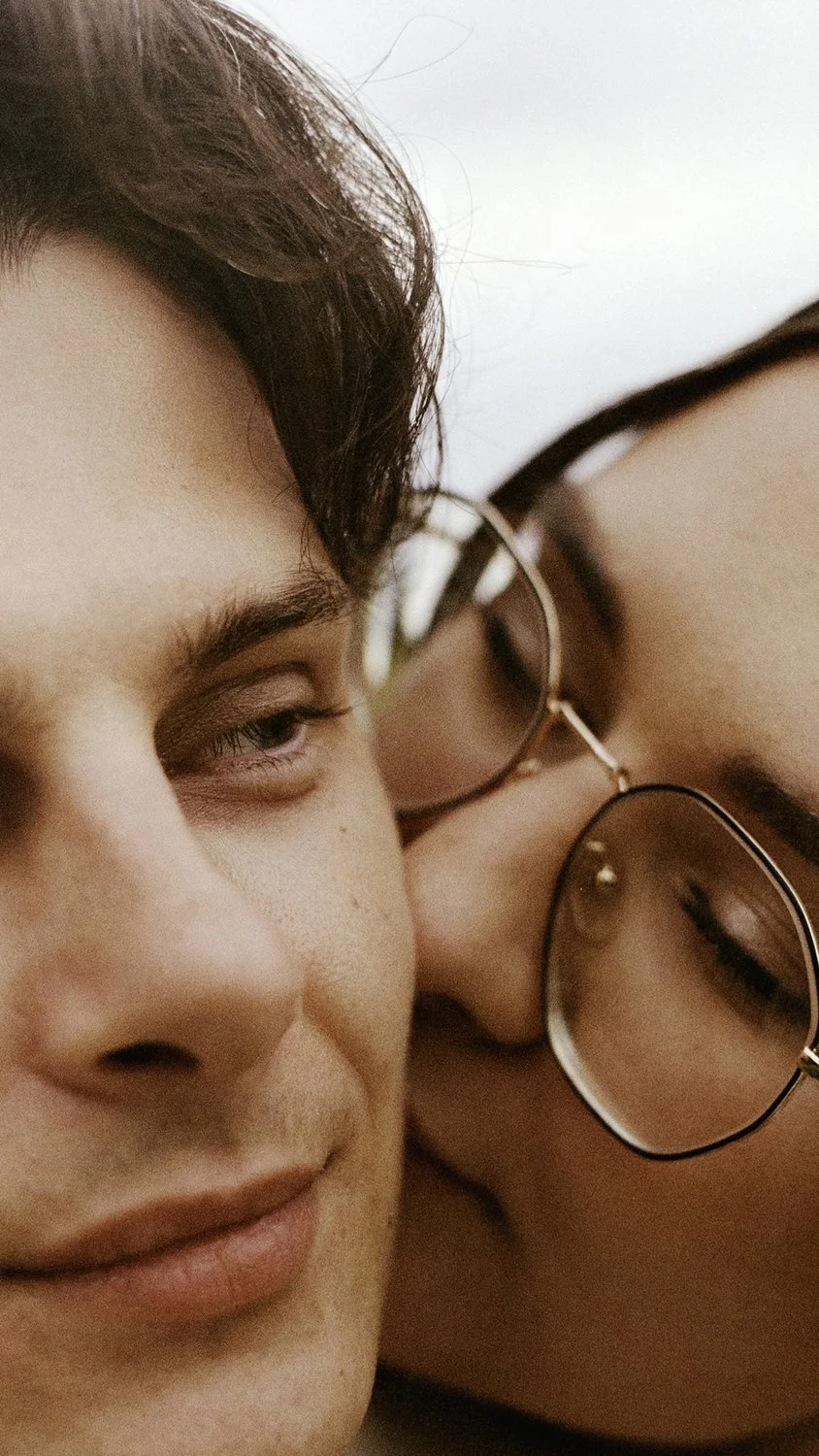 Close-up of two young people with their heads touching, one wearing glasses, both with relaxed expressions.