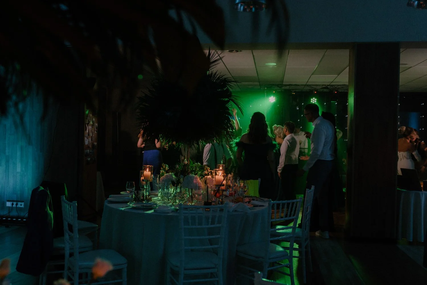 People dancing and socializing at a reception with a decorated table and green lighting.