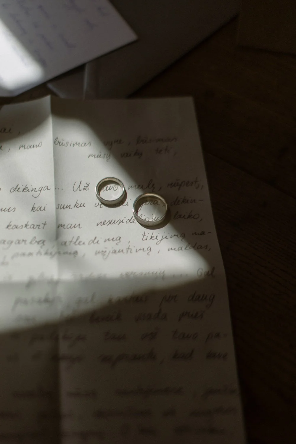 Two rings placed on a handwritten letter with a shadow cast over part of the paper, on a wooden surface.