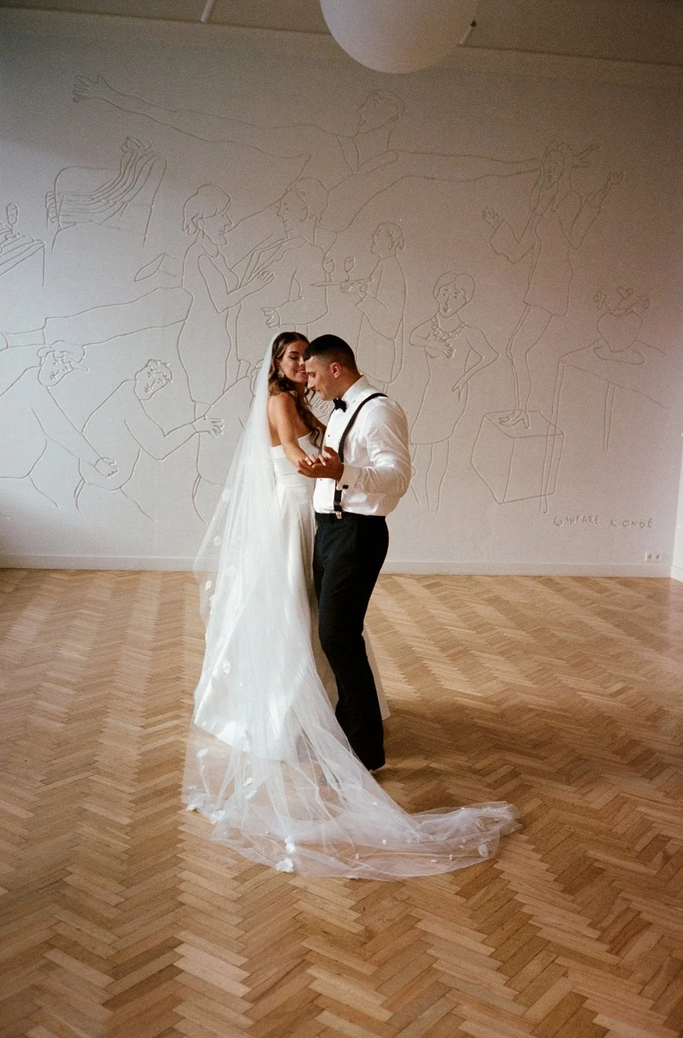 A bride and groom dancing together in a photo on their wedding day, with a wall of line art drawings in the background.