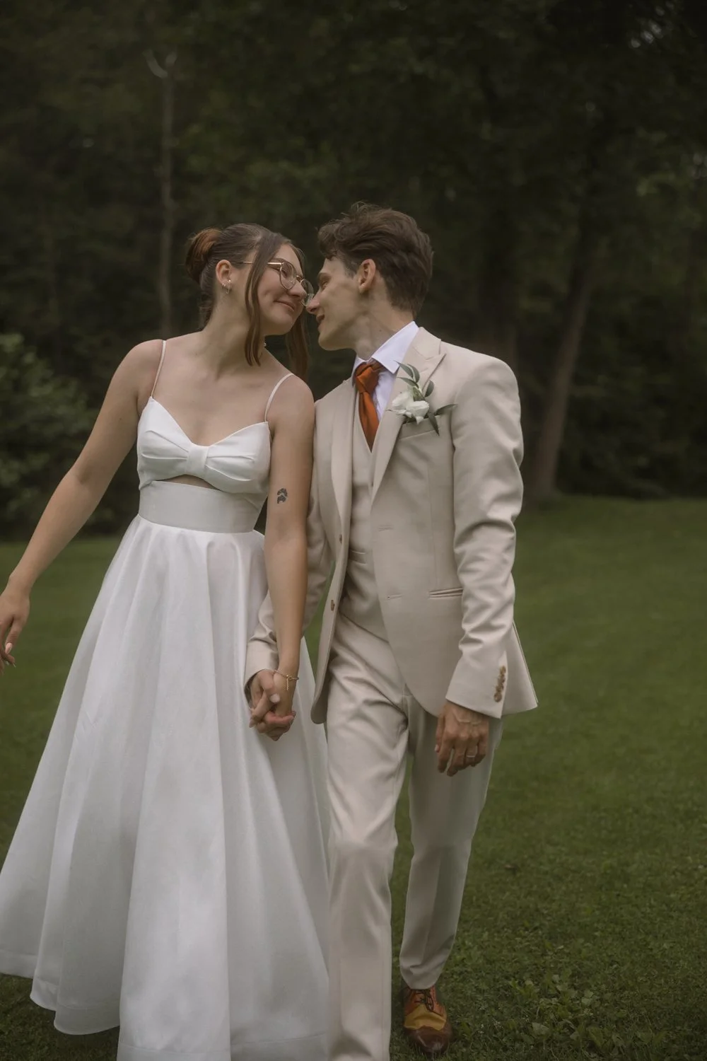 A bride and groom holding hands and touching foreheads outdoors during their wedding, with trees in the background.
