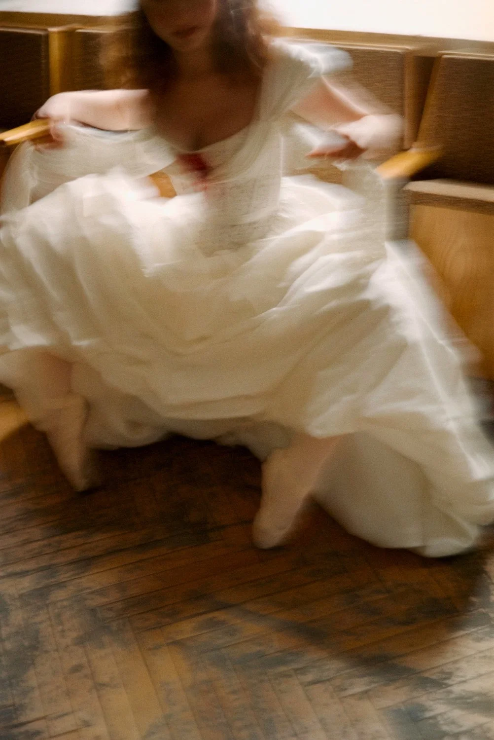 A person in a white dress sitting with her legs apart on a wooden floor, with a blurred background and motion effects.