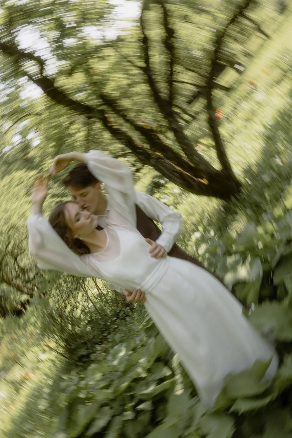 A couple dressed in white, dancing together outdoors in a lush green forest, with a motion blur effect.