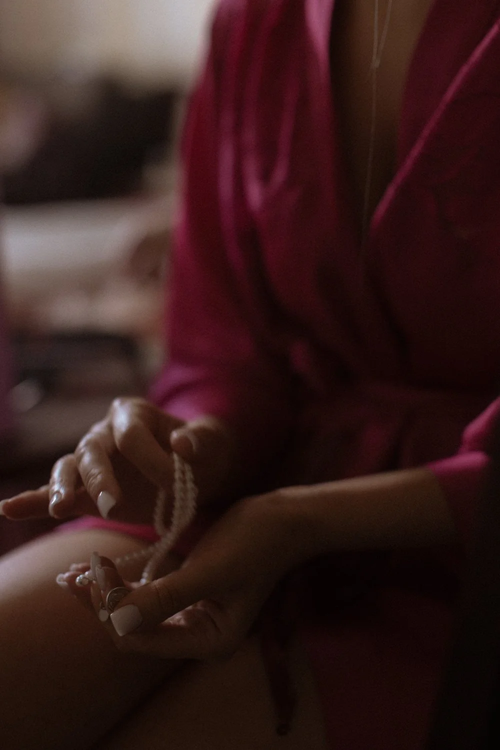 Close-up of a person in a pink outfit holding loose pearls, with their hands gently clasped.