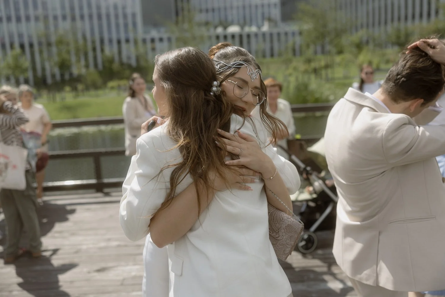 Two women hugging each other at an outdoor event, surrounded by other people and city buildings in the background.