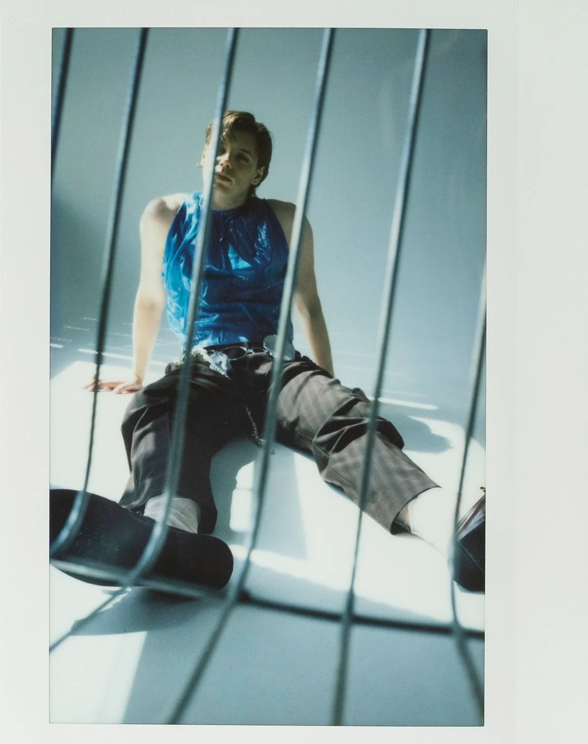 A young man with brown hair and light skin sitting on the floor inside a white bathtub, viewed through a metal wire gate.