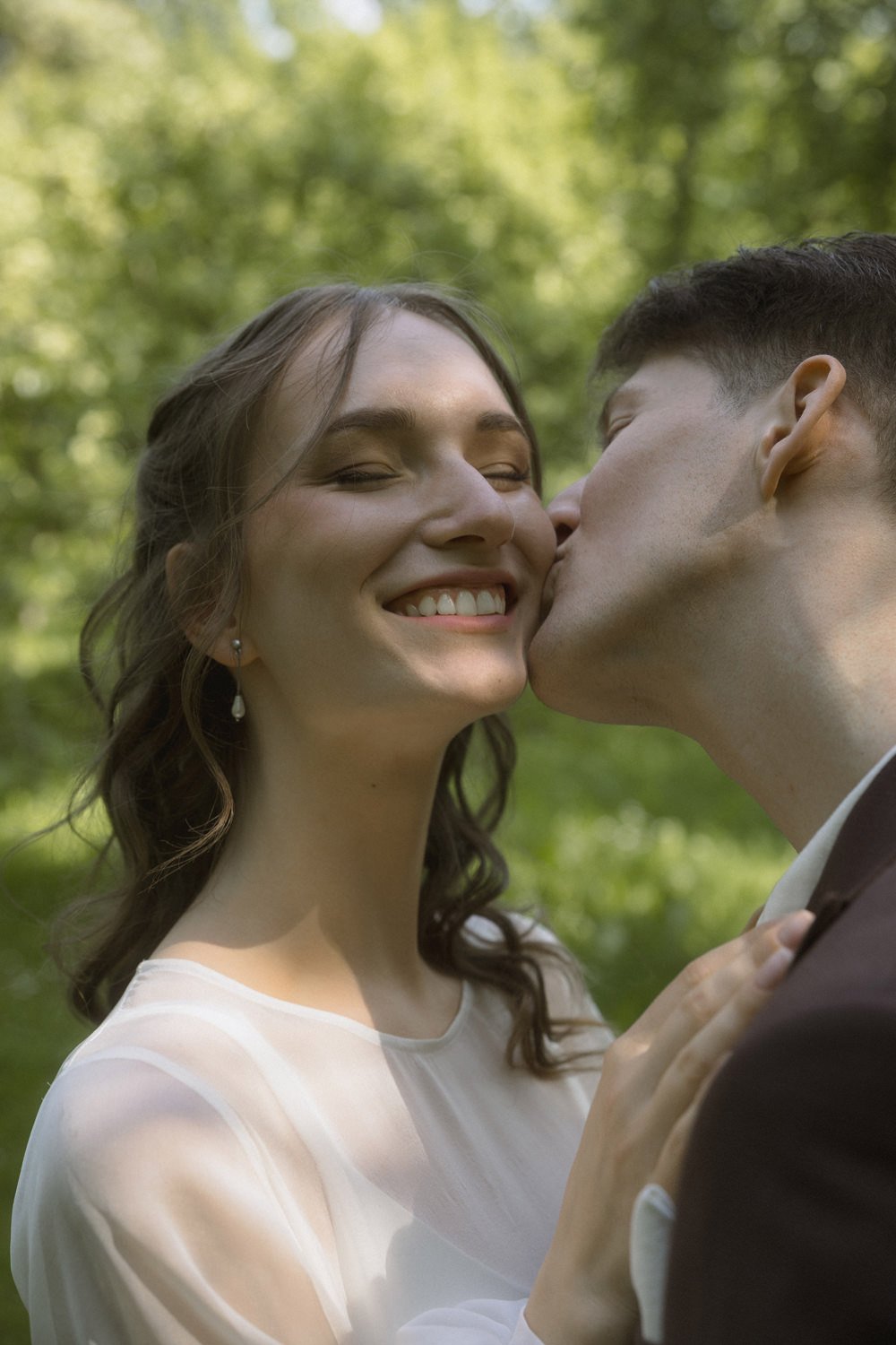 A woman smiling happily as a man kisses her cheek outdoors.
