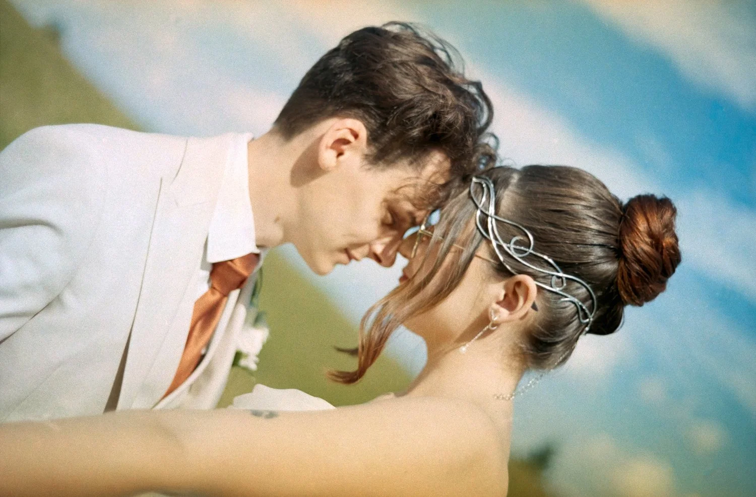 A couple is touching foreheads close together outdoors with a blue sky background.