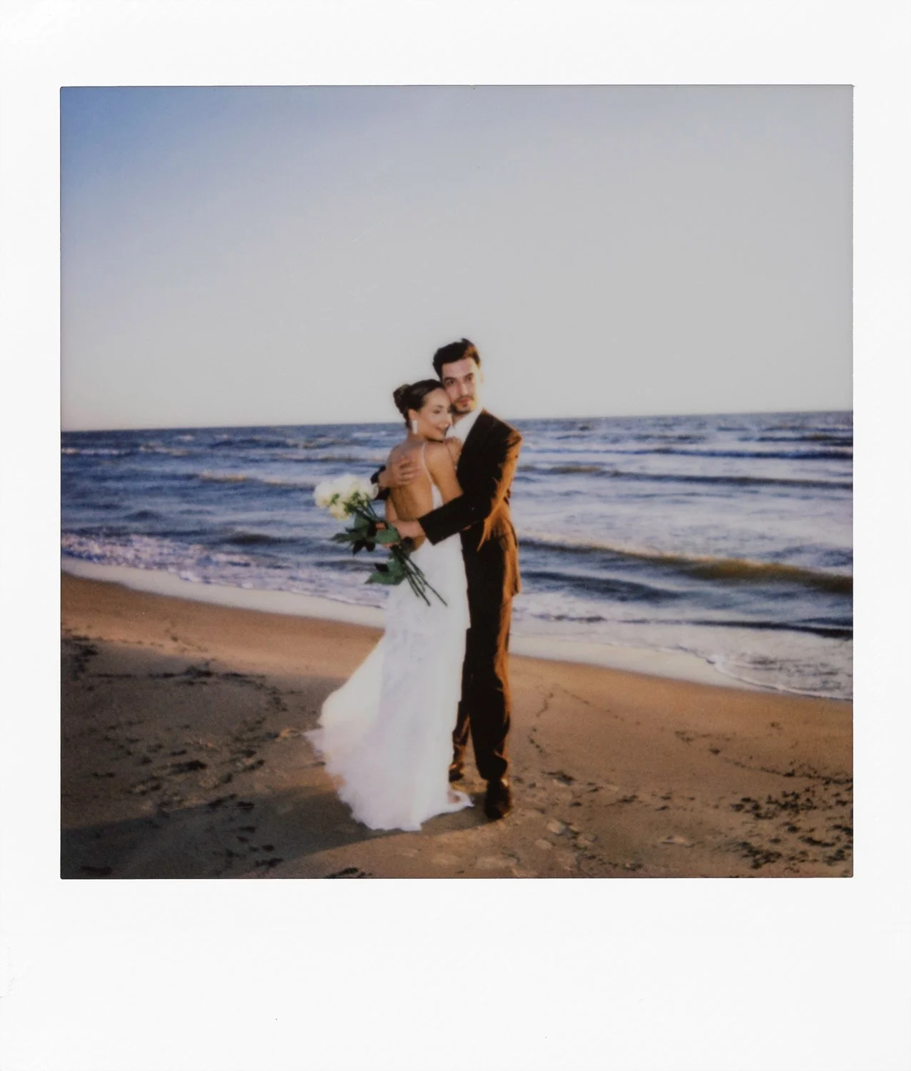 A newlywed couple embracing on a beach with the ocean in the background.